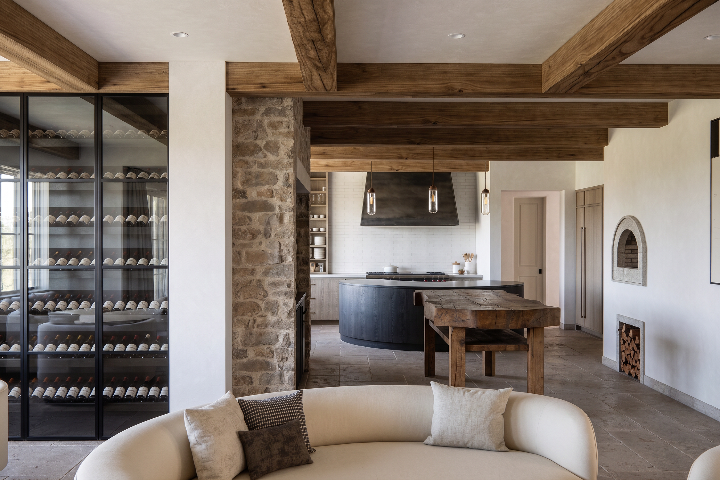 Modern kitchen and living room with wood beams, wine fridge, and stone fireplace.