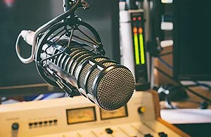 Close-up of a professional microphone in a recording studio with audio equipment in the background.