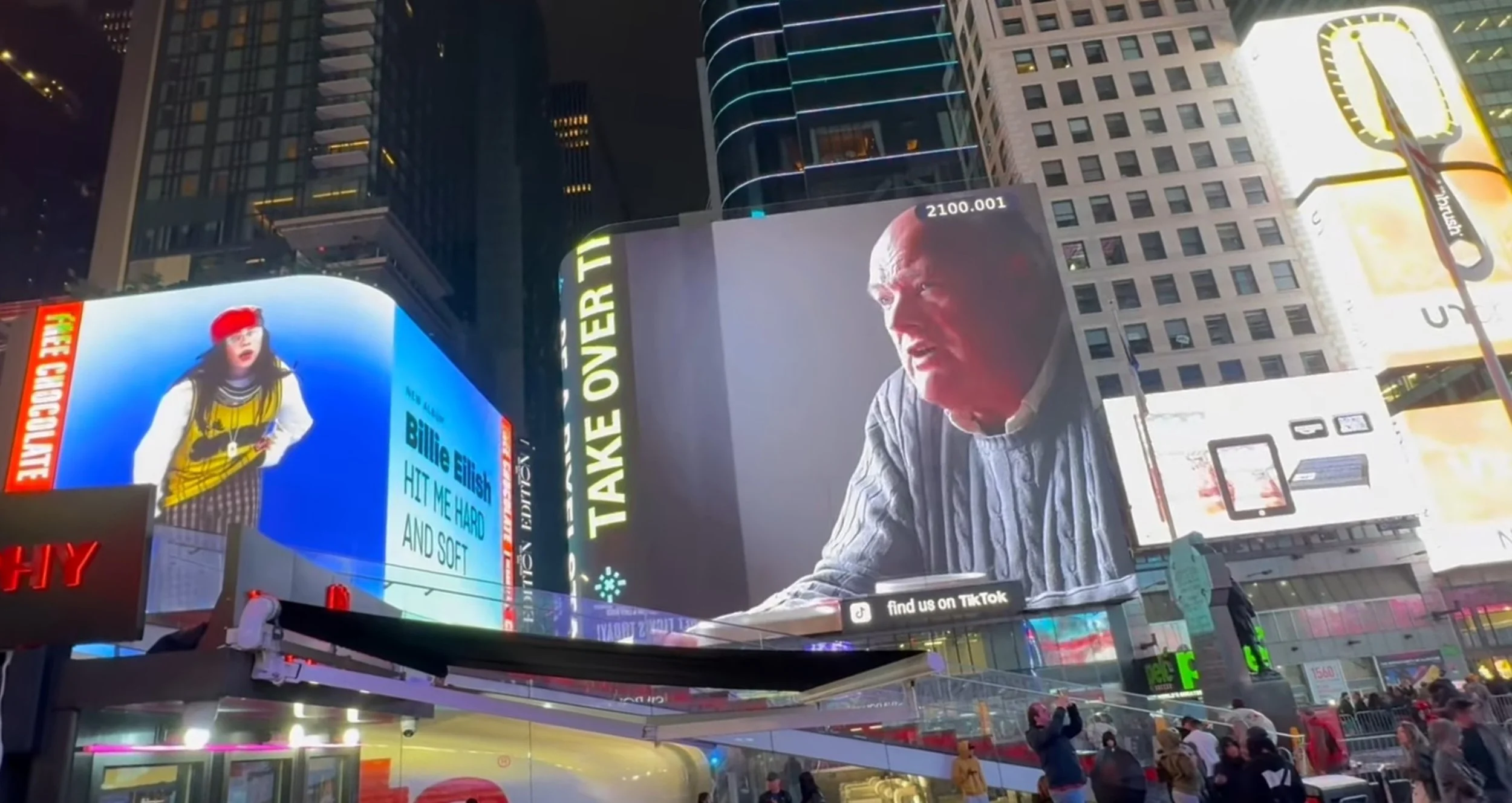 Nighttime scene in Times Square, New York City, with illuminated billboards, electronic advertisements, and a crowd of people on the street.