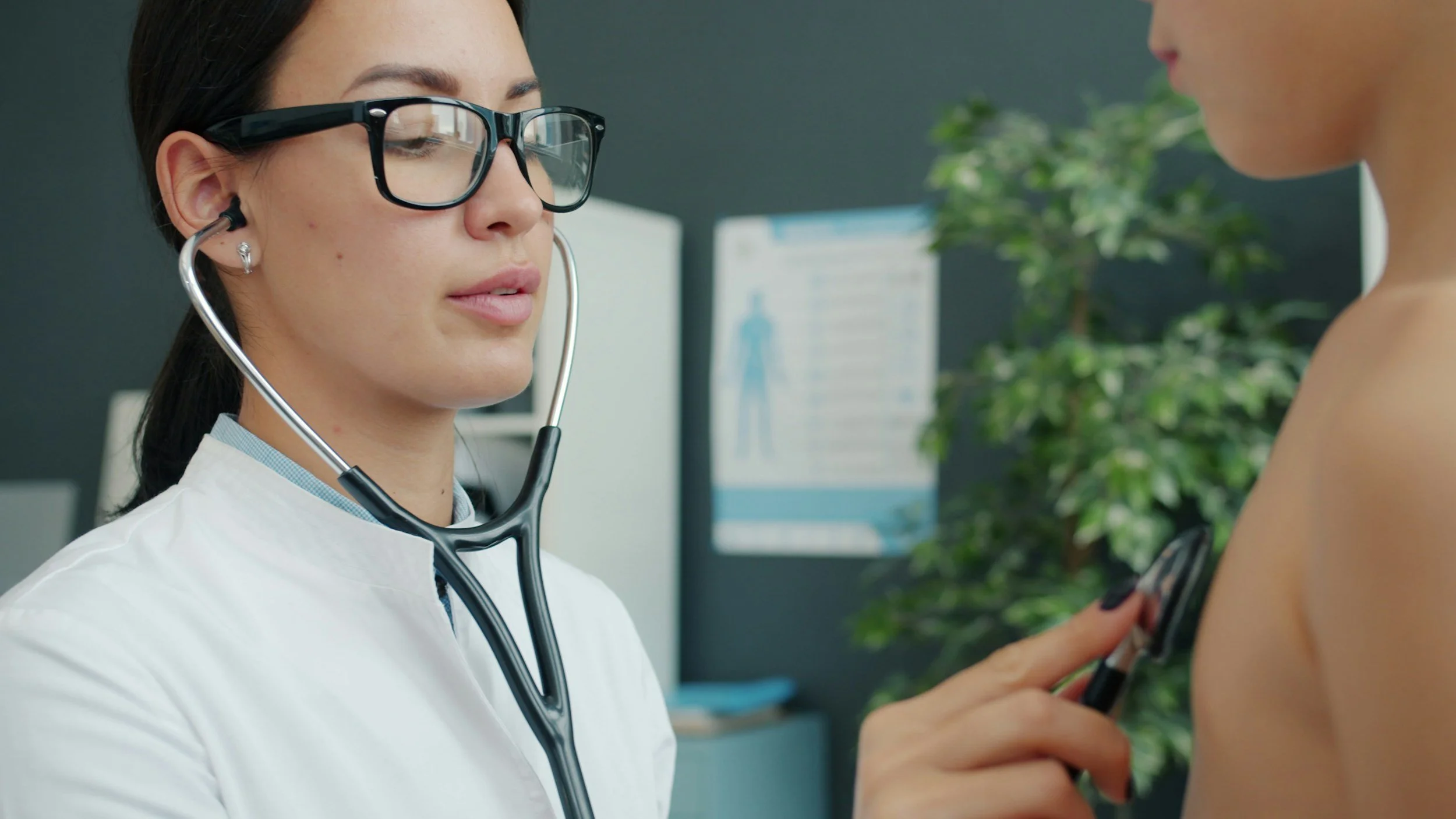 A medical professional providing pediatric care by using a stethoscope to check the young patient's heart in a medical office.