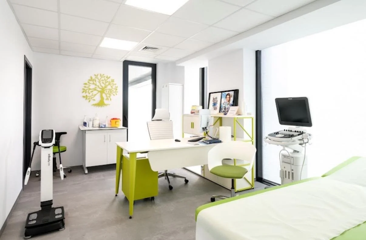 Moderne Arztpraxis mit Schreibtisch, Patientenbett, Computer, medizinischem Equipment und Dekorationen.