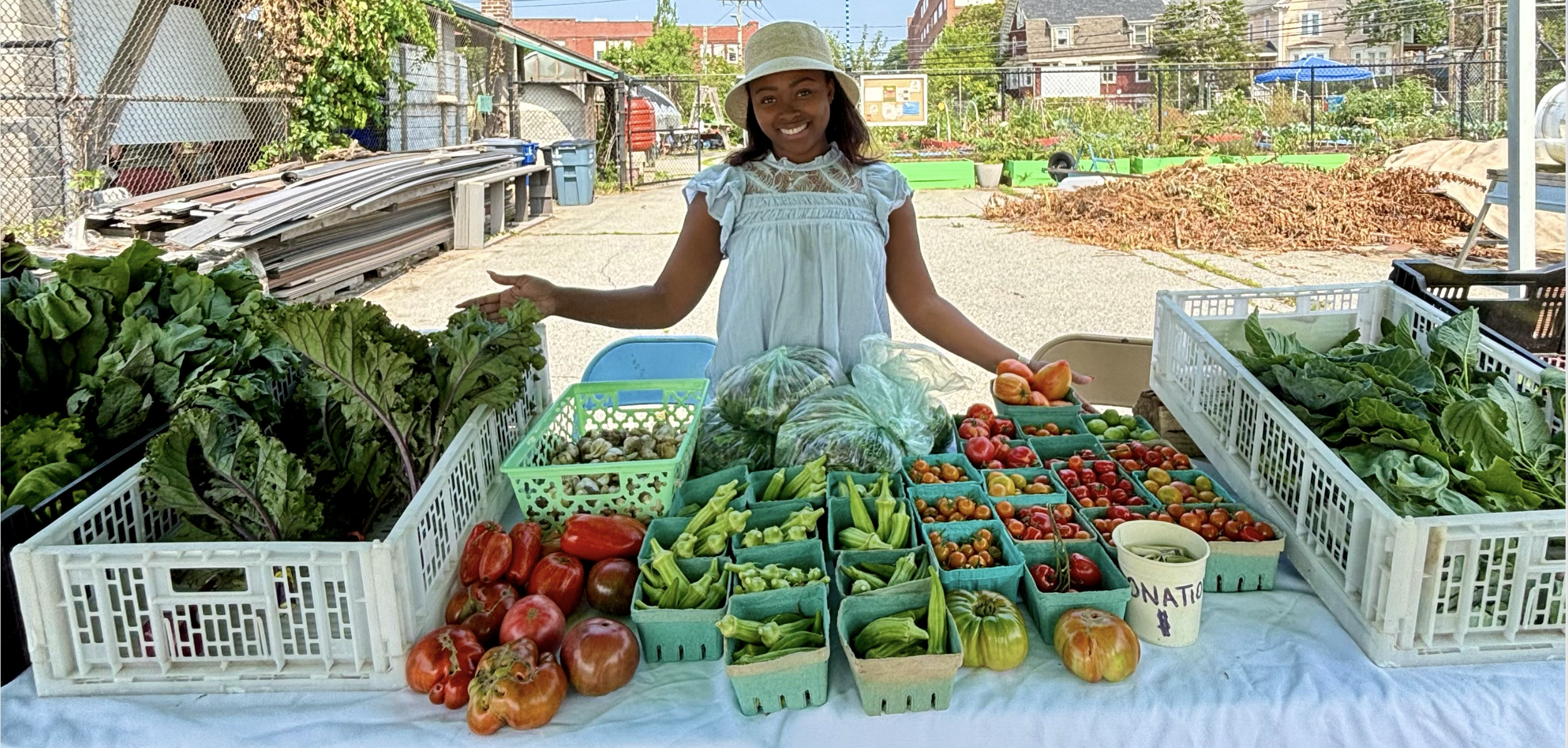 Vetiveah stands behind a table filled with fresh vegetables at an outdoor market.