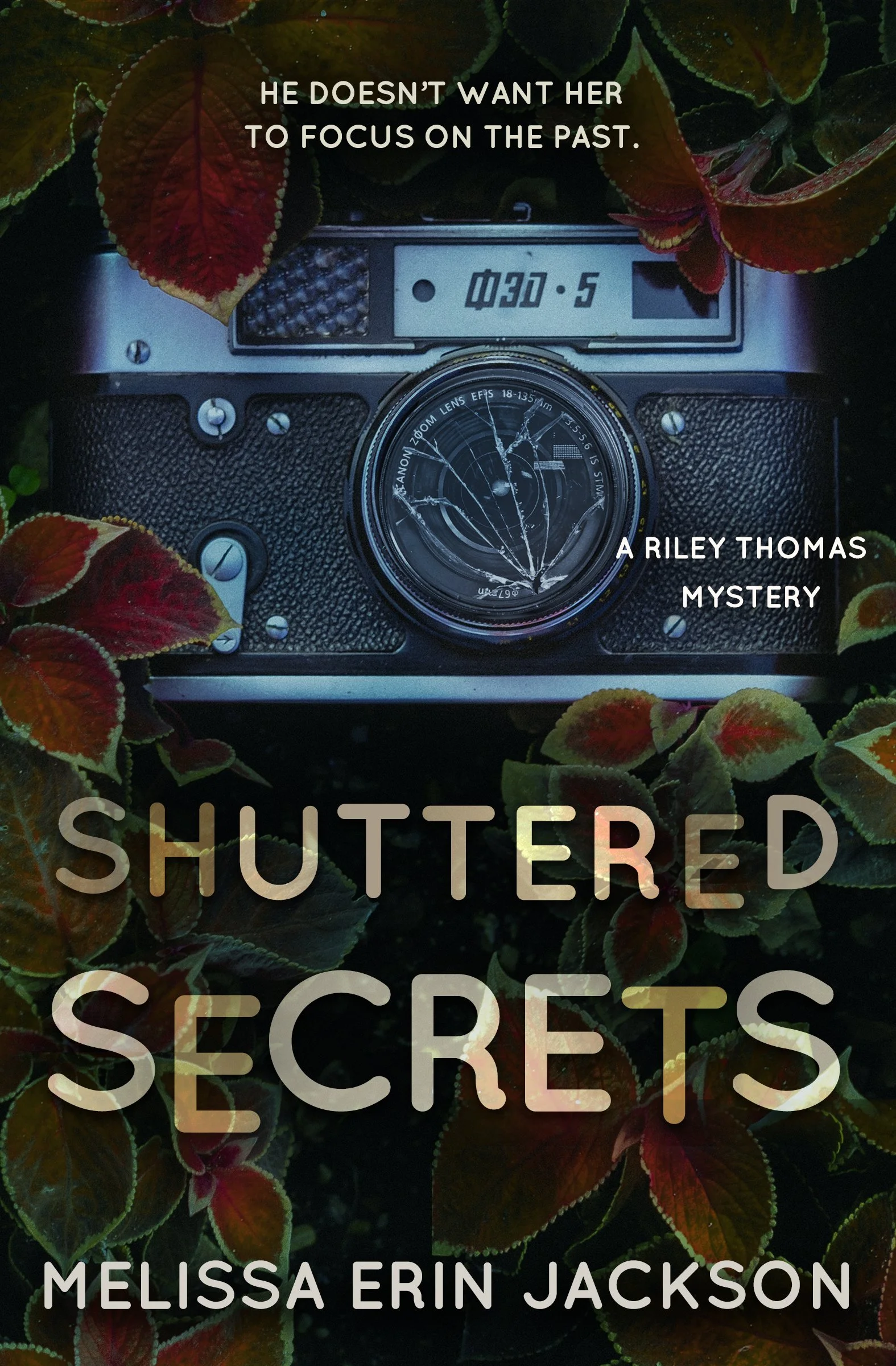 A vintage camera is surrounded by colorful leaves, with text overlay reading: "He doesn’t want her to focus on the past. A Riley Thomas Mystery. Shuttered Secrets. Melissa Erin Jackson."