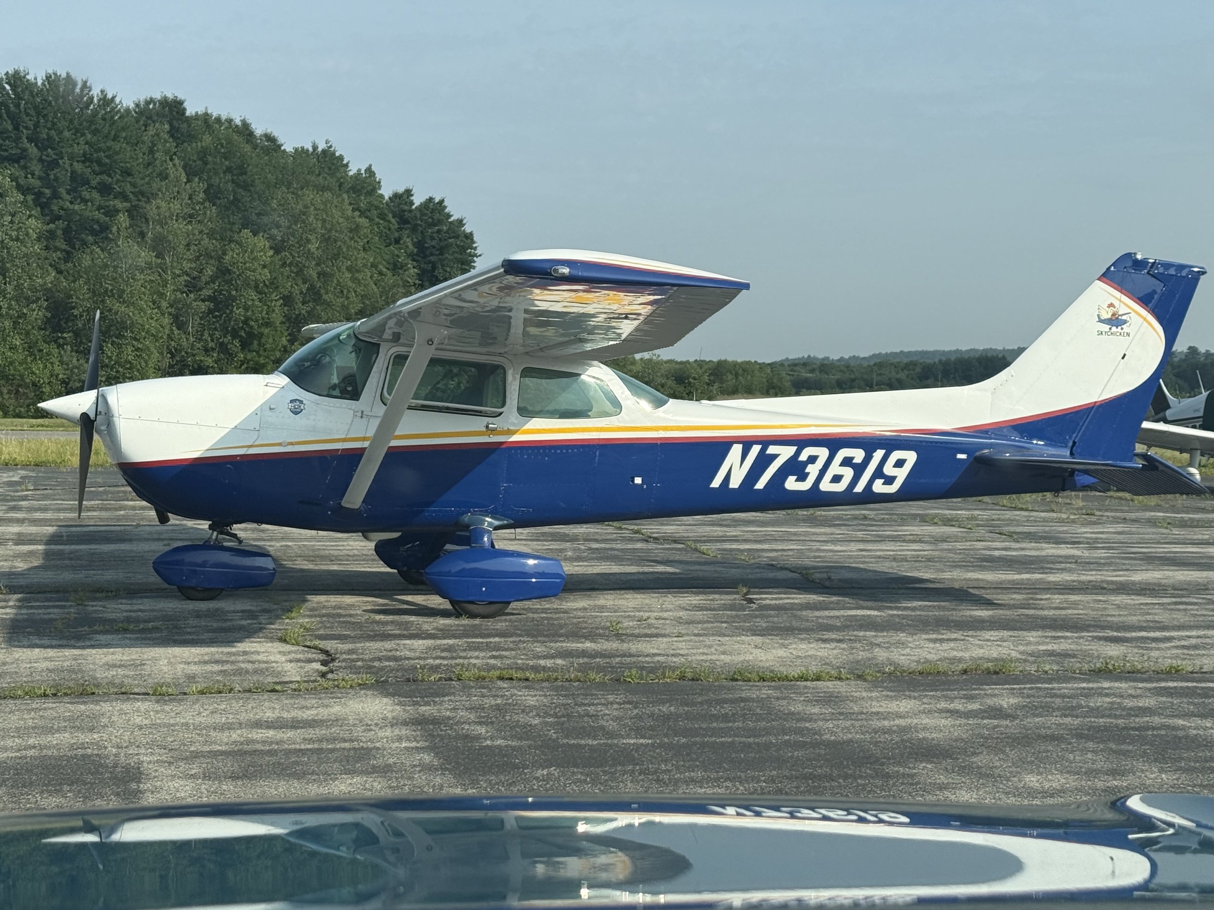 Small private propeller airplane on runway with green trees and blue sky in the background.