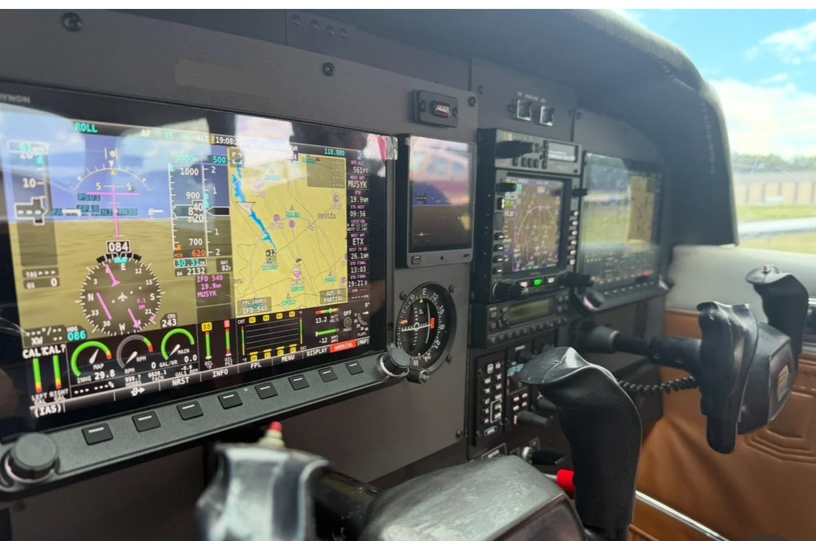 Cockpit of a small airplane showing multiple digital navigation and control screens, with a view of the runway and blue sky outside.