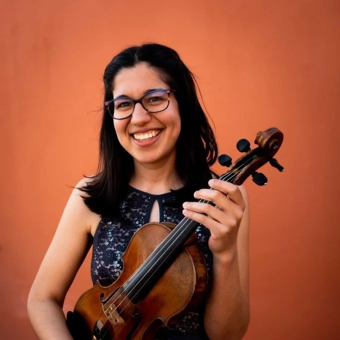 Smiling woman with glasses holding a violin against an orange background.