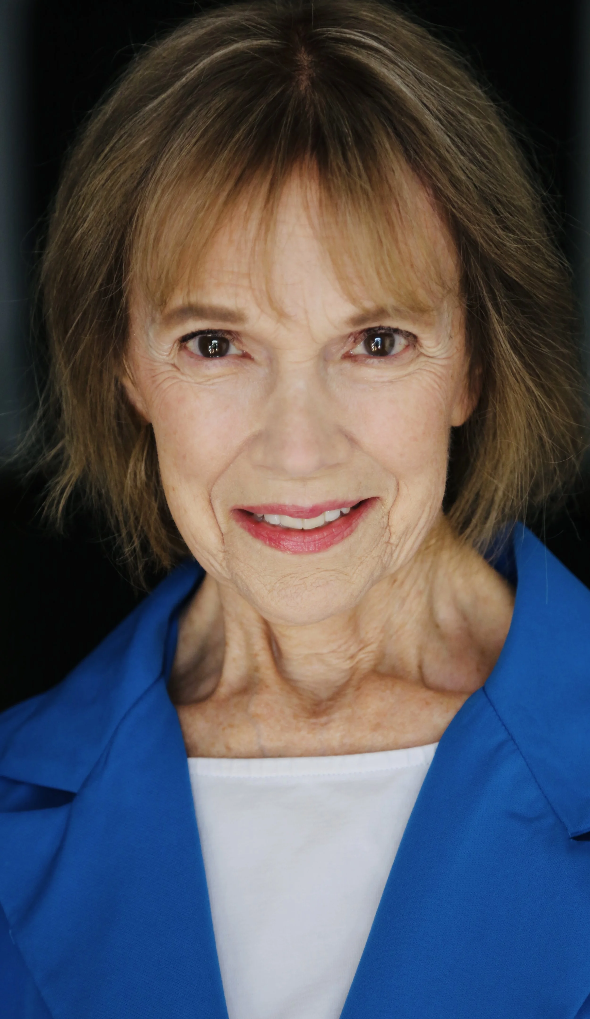 A close-up portrait of Mary O' Kerrigan with short brown hair, wearing a blue jacket and a white top, smiling and looking at the camera.