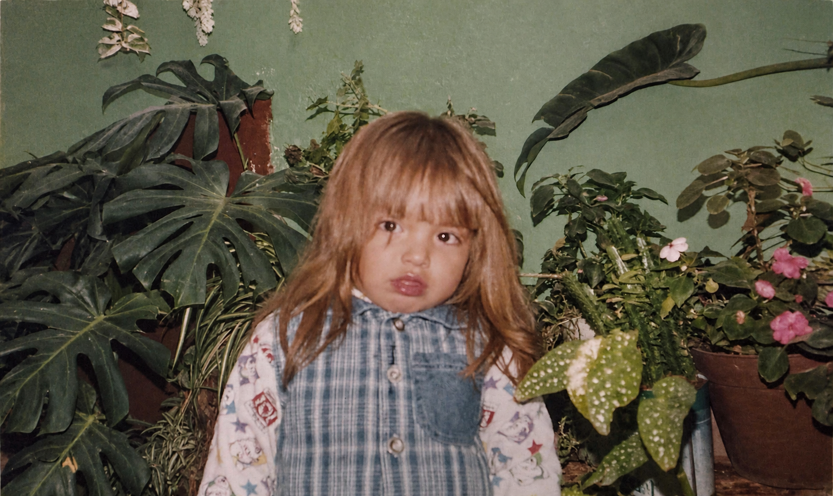 A childhood photograph of Kimberly surrounded by lush houseplants.