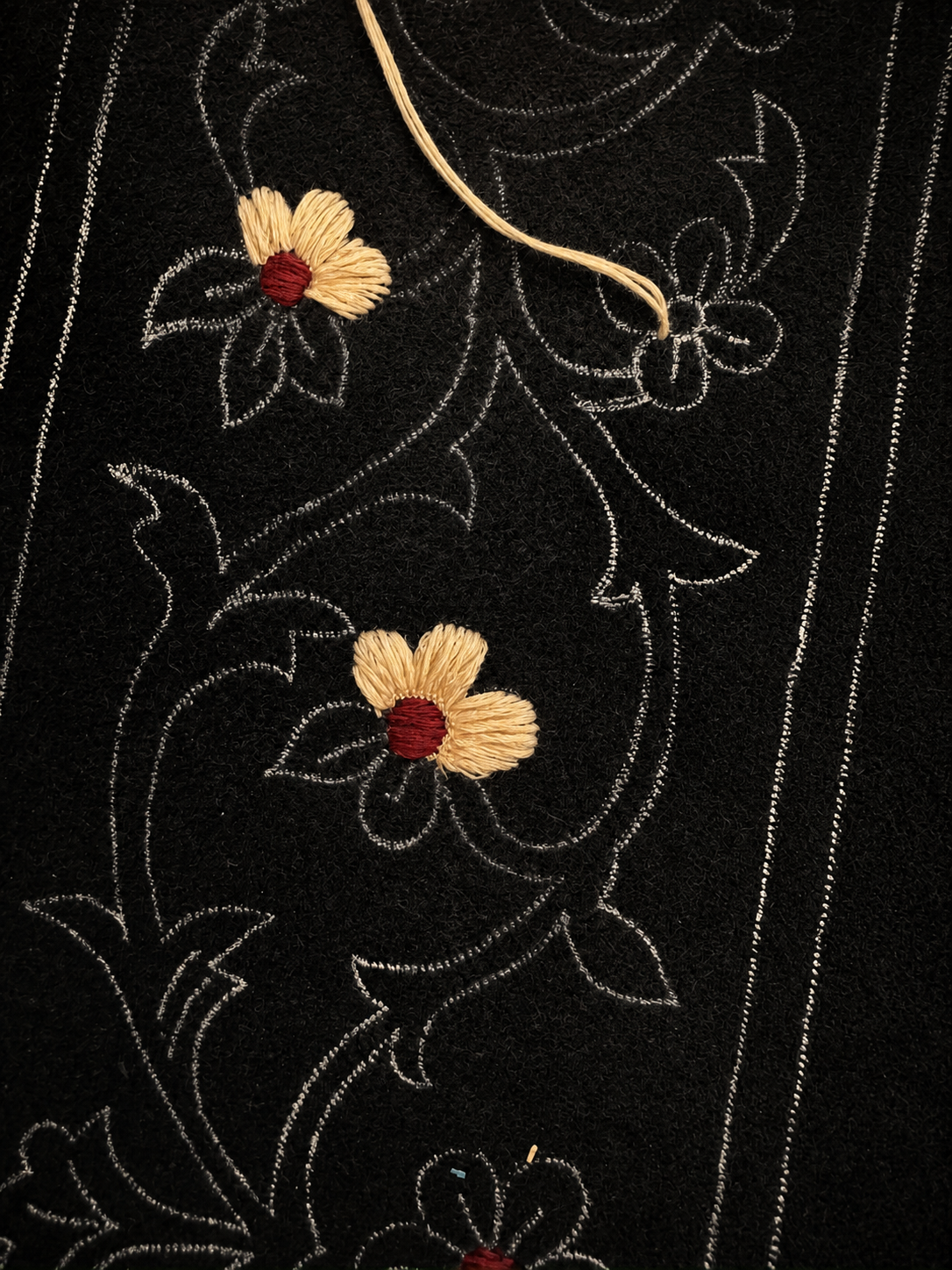 Black fabric with white embroidery of floral and leaf patterns, decorated with two 3D embroidered yellow flowers with red centers.