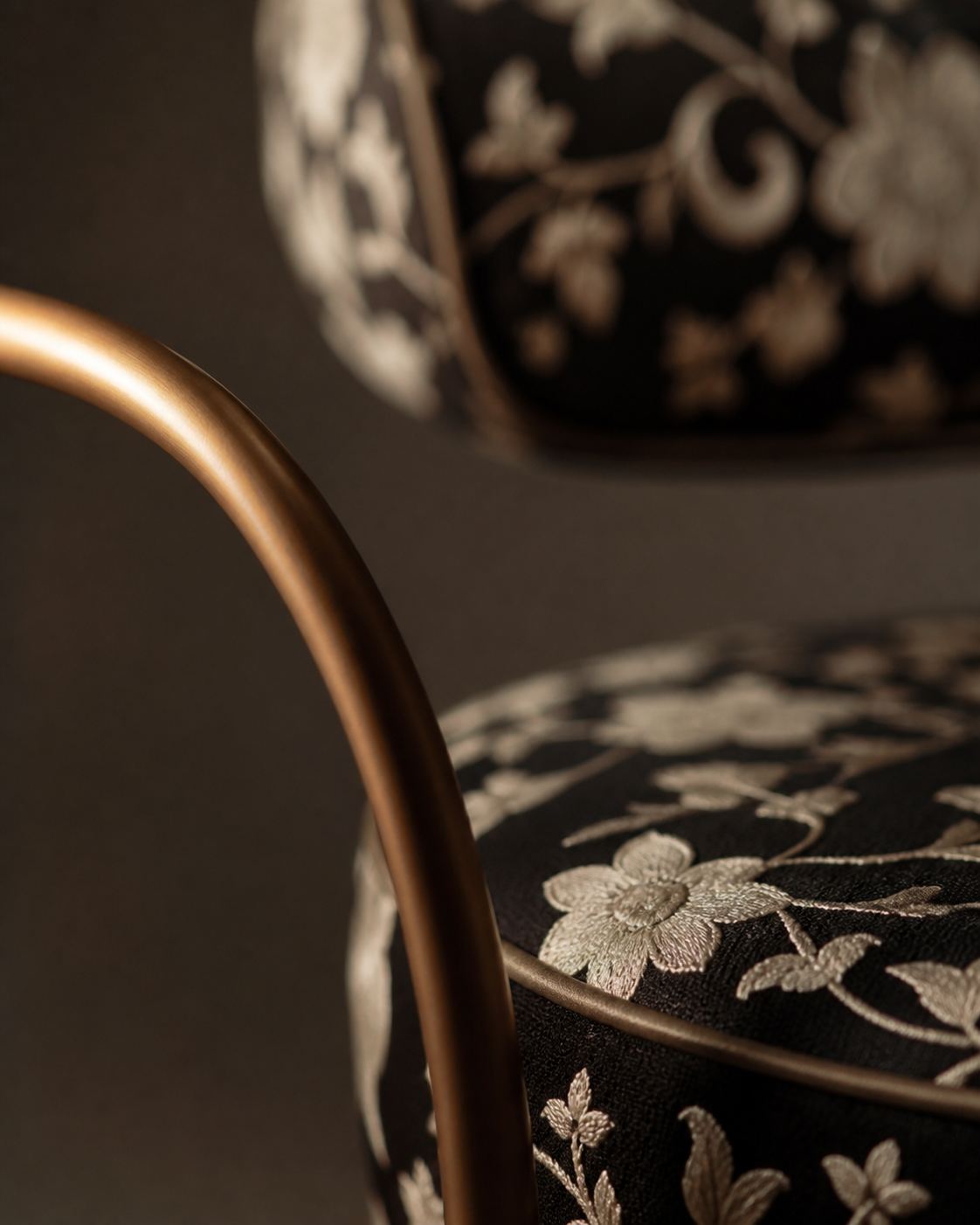 Close-up of a chair with black upholstery embroidered with gold floral patterns, and a rounded metal frame.