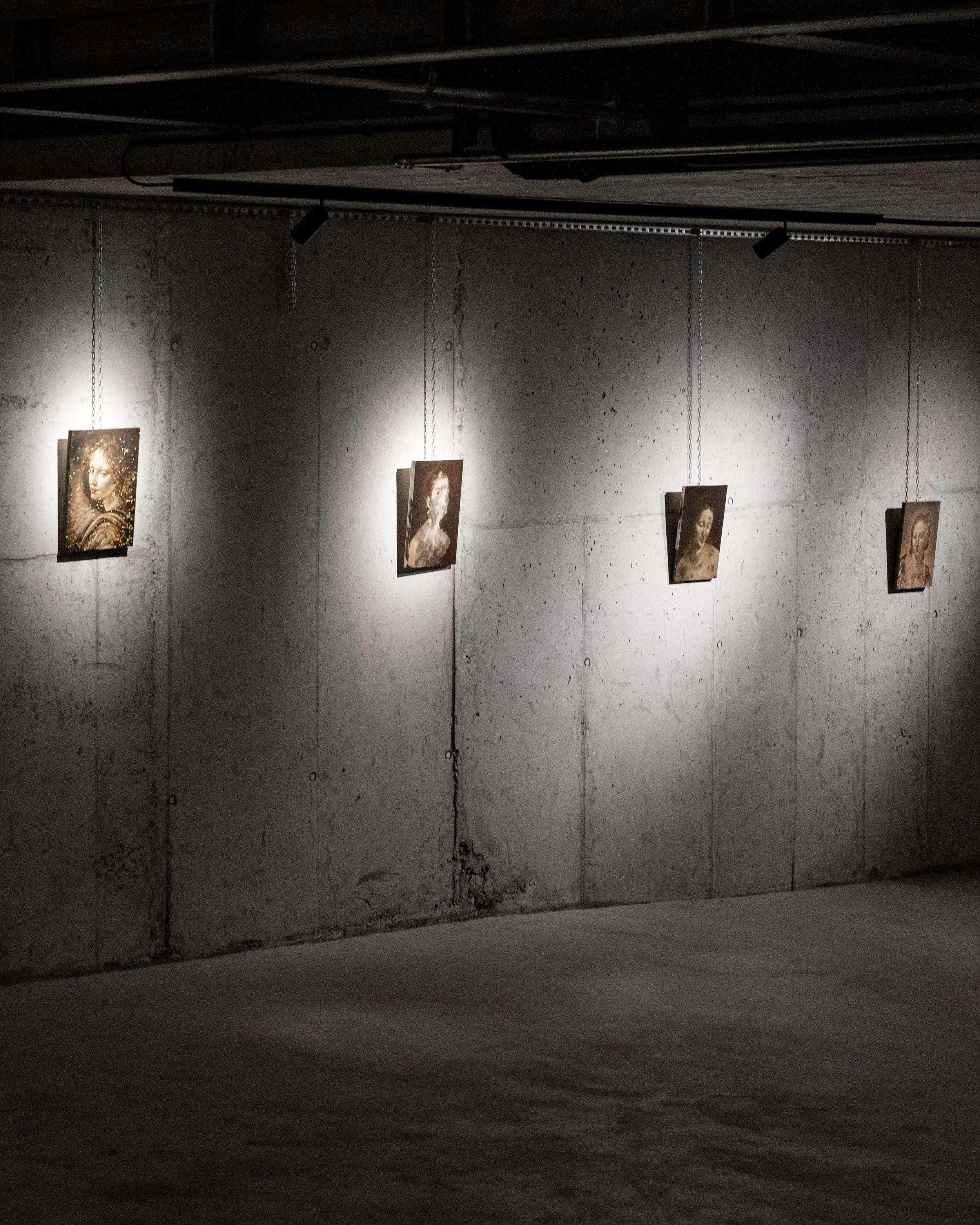 Dark gallery with portraits of women illuminated by spotlights on a concrete wall.