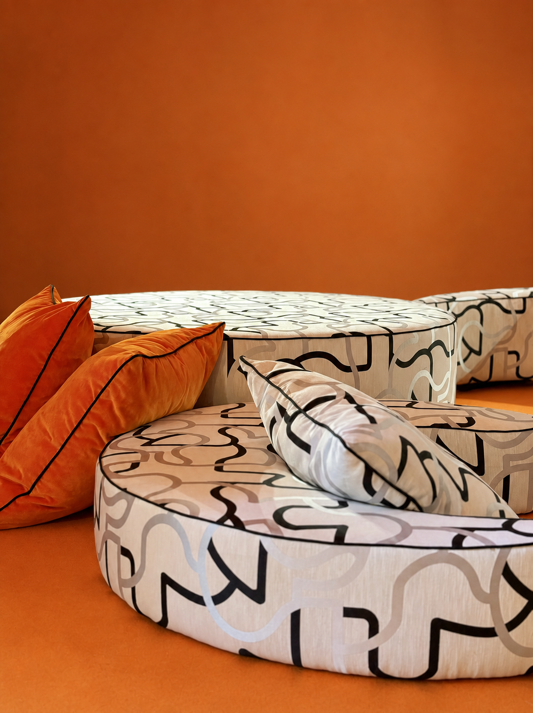 Round beds with abstract black and white patterns and orange velvet pillows on an orange carpeted floor against a solid orange wall.
