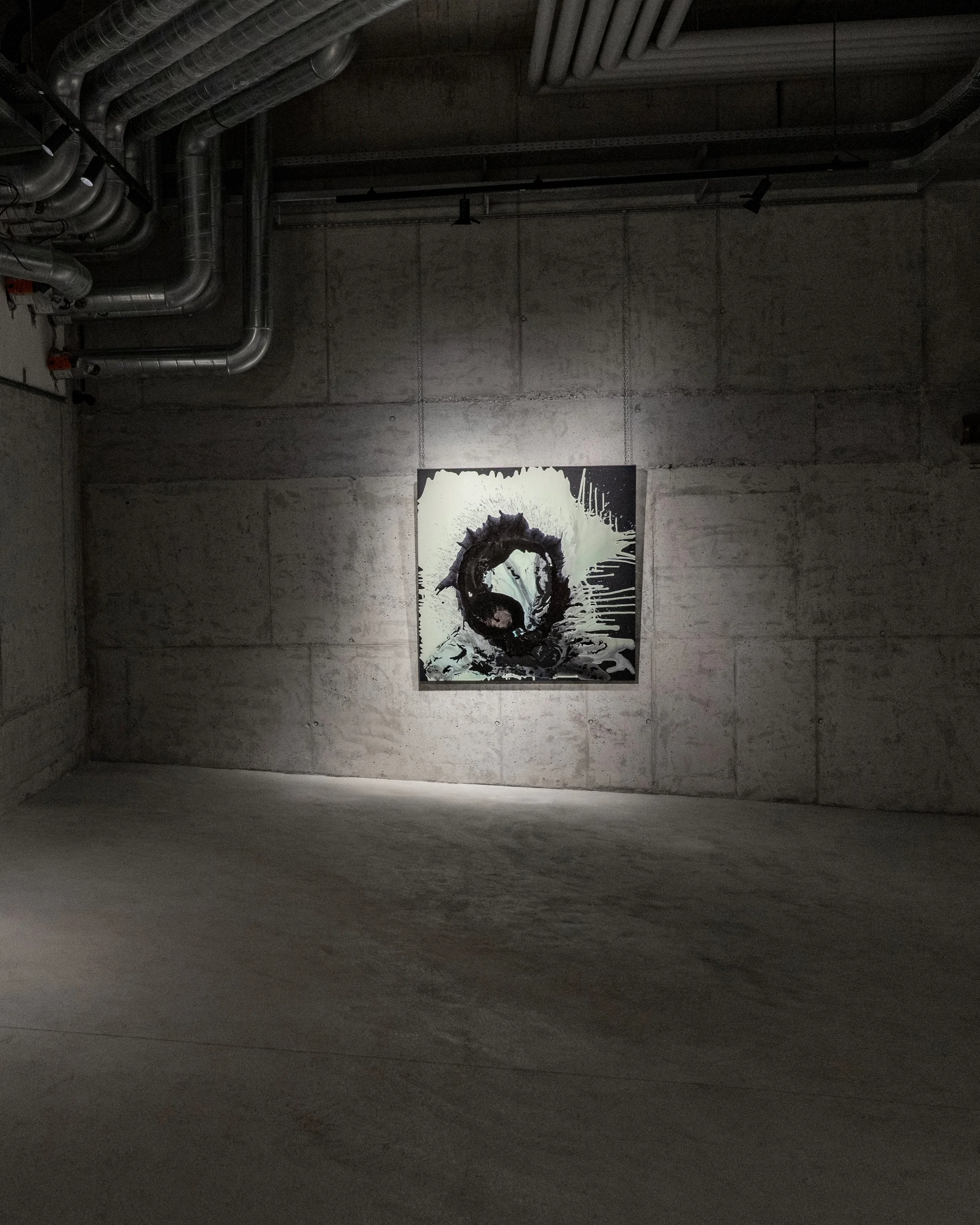 Contemporary art gallery with gray concrete walls and ceiling, showcasing a black and white abstract painting of a swirling shape, illuminated by ceiling lights.