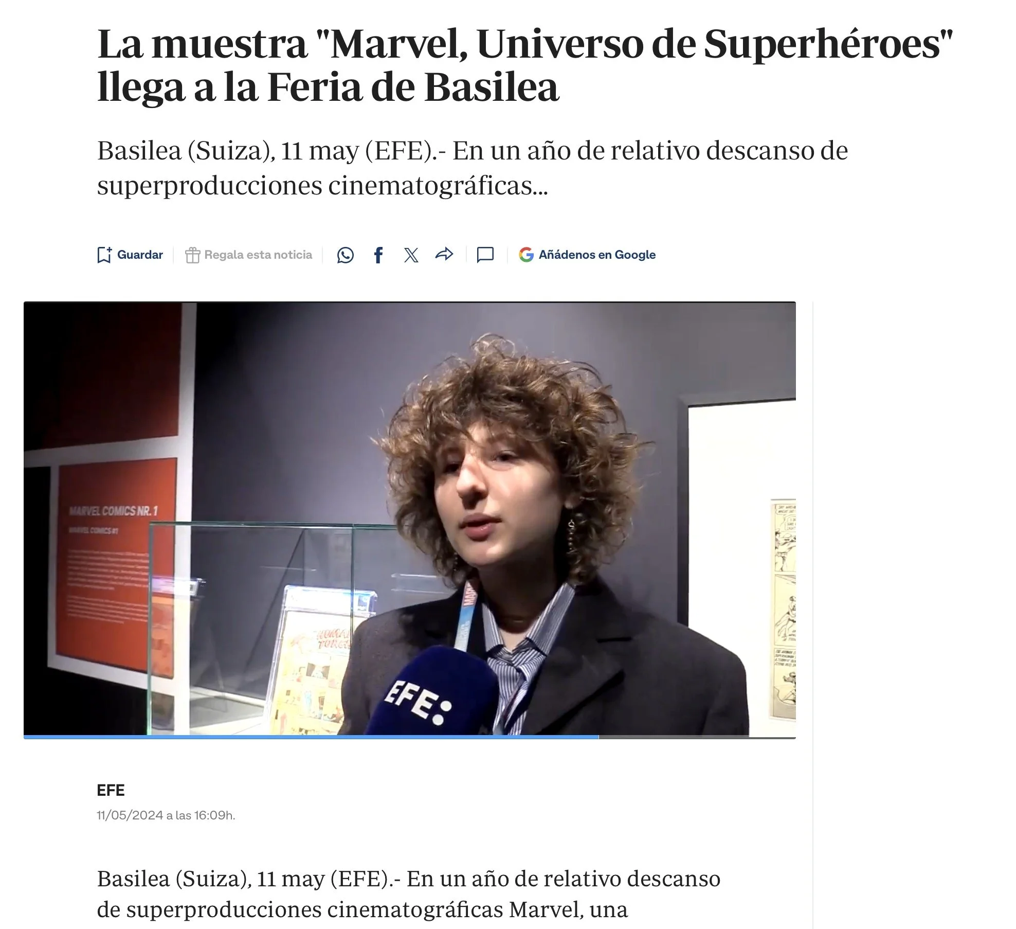 A woman being interviewed at a Marvel exhibition, with display panels and Marvel comic posters in the background.