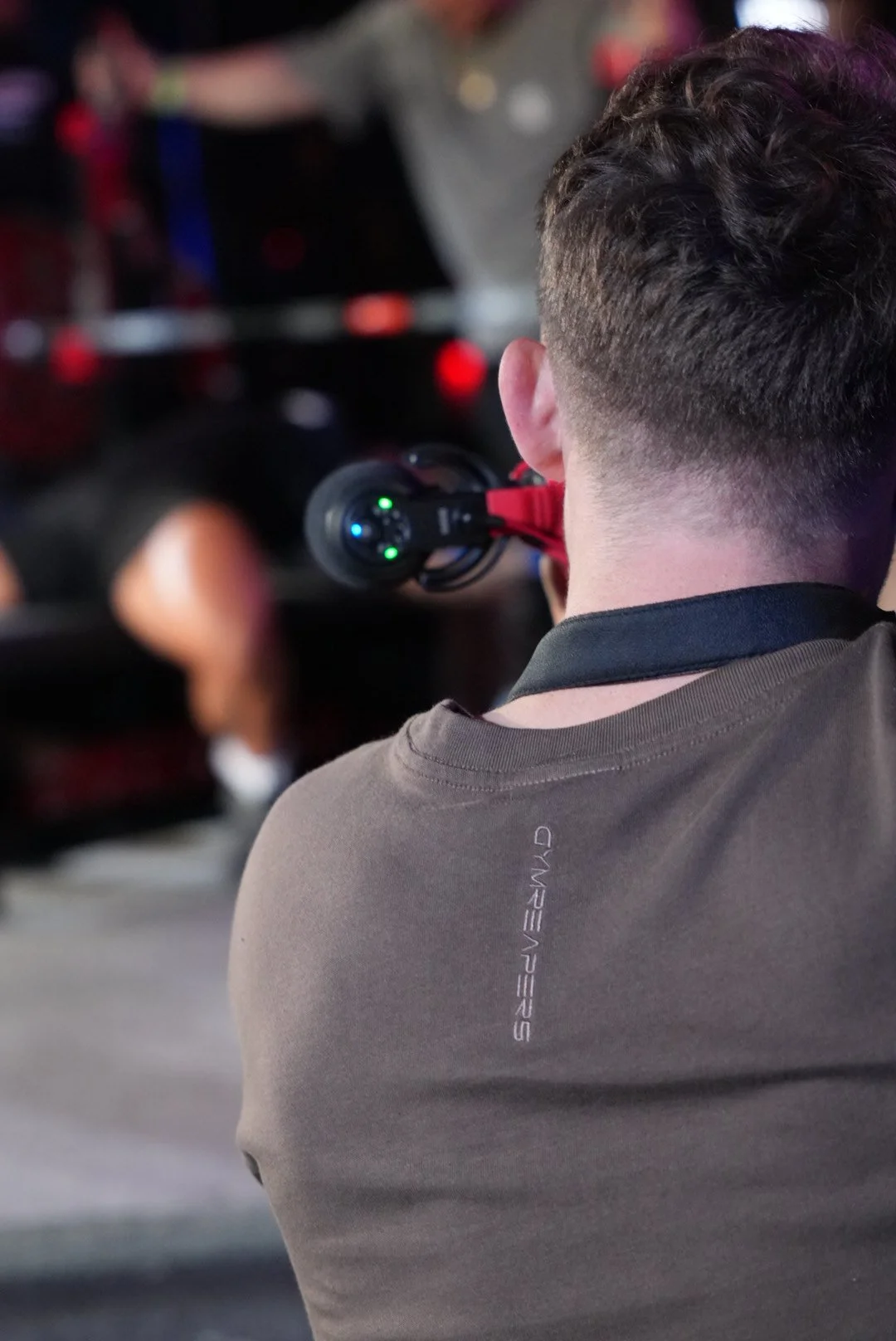 Person with short dark hair wearing a grey t-shirt, holding a laser tag gun in a dark room with blurry background.