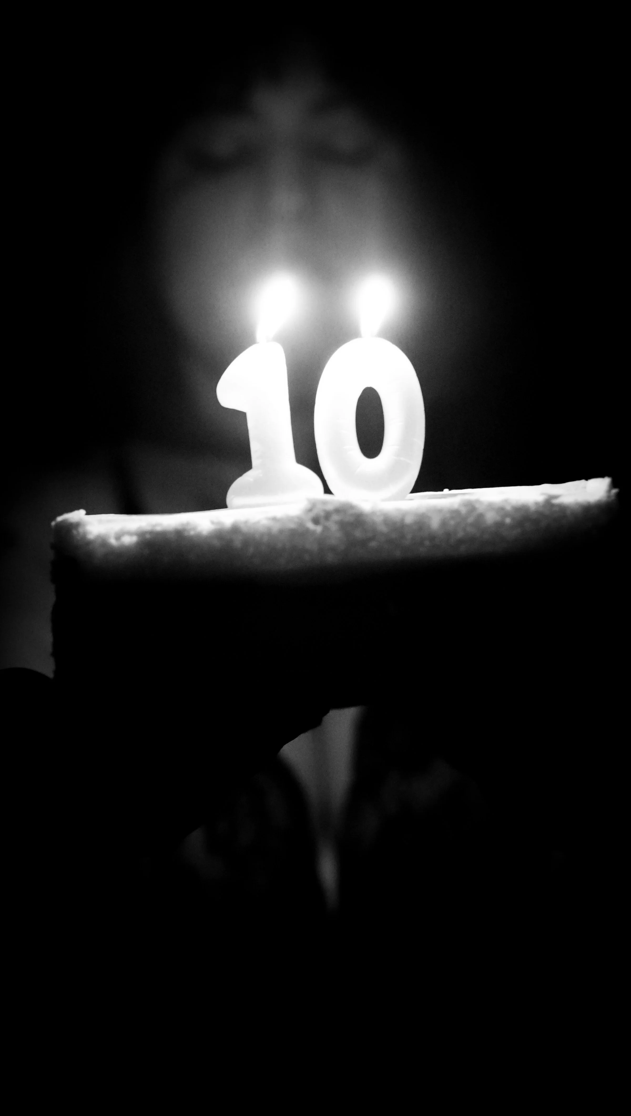 A calendar cake with a birthday candle shaped like the number 10, held on a person's hand in a dark environment.