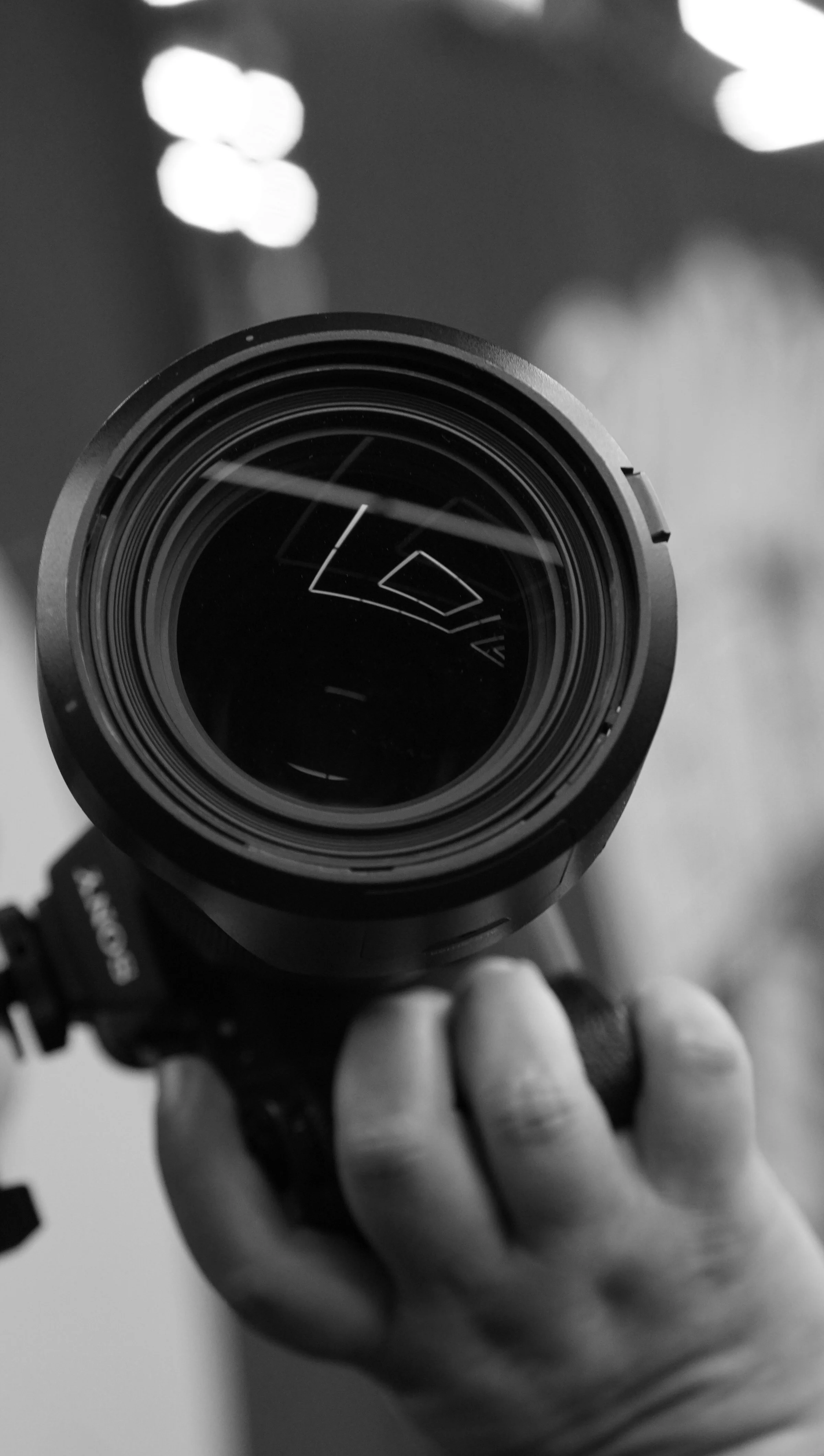 Close-up of a camera lens being held by a person's hand in black and white.