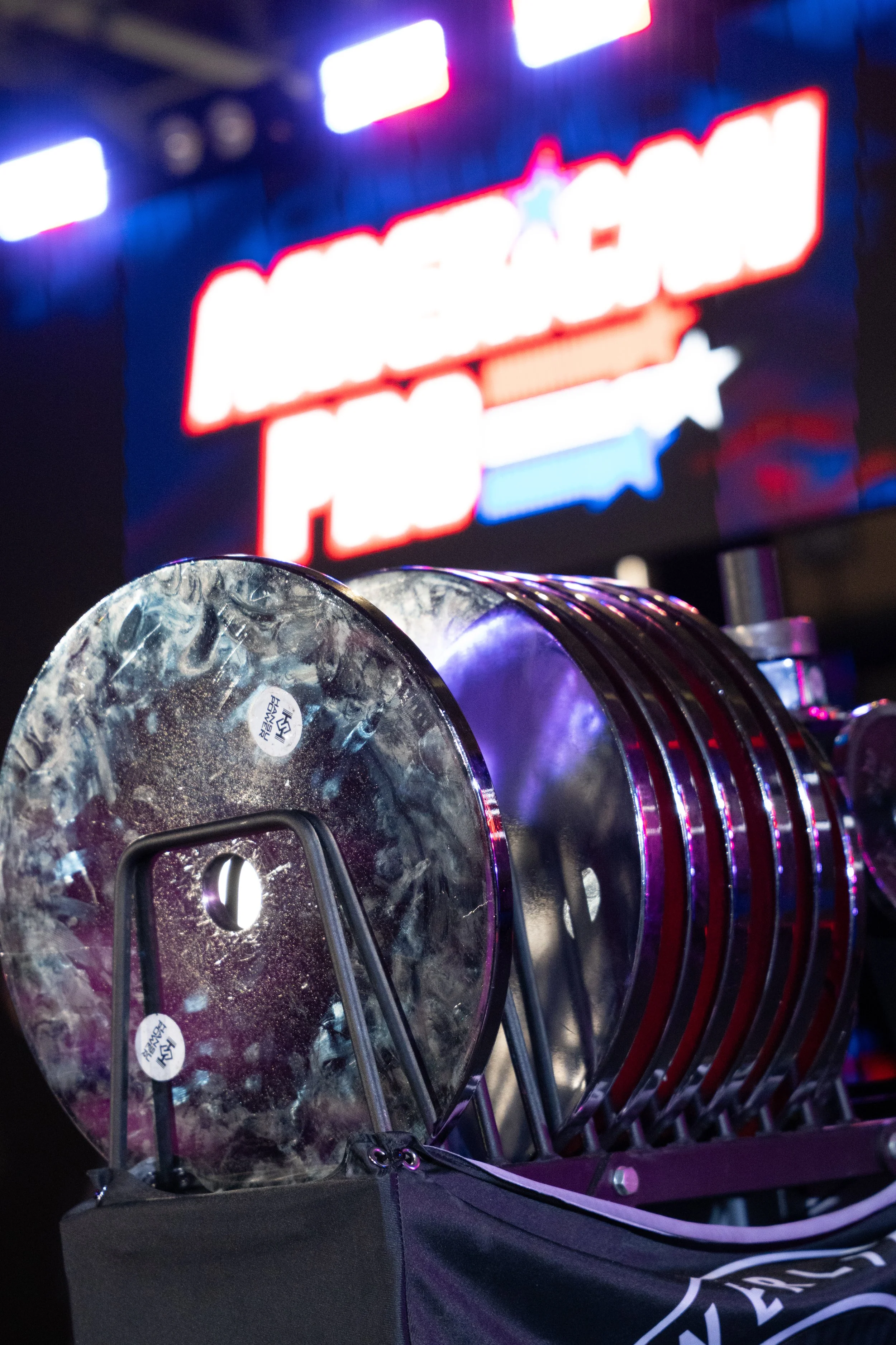 Row of ice hockey pucks in a black hockey puck holder, with a brightly lit electronic billboard in the background.