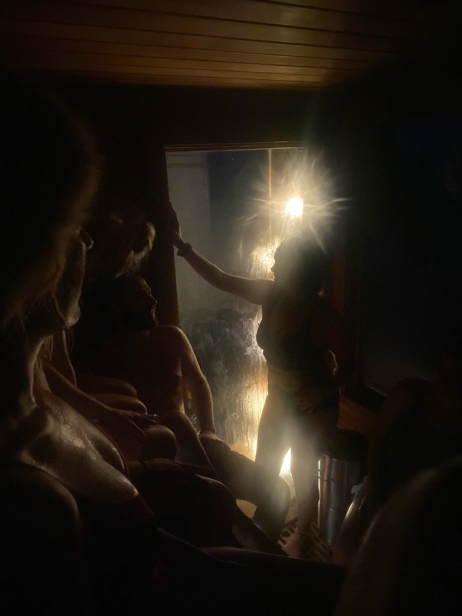 People gathered in a dark, steamy room illuminated by a bright light through a window.
