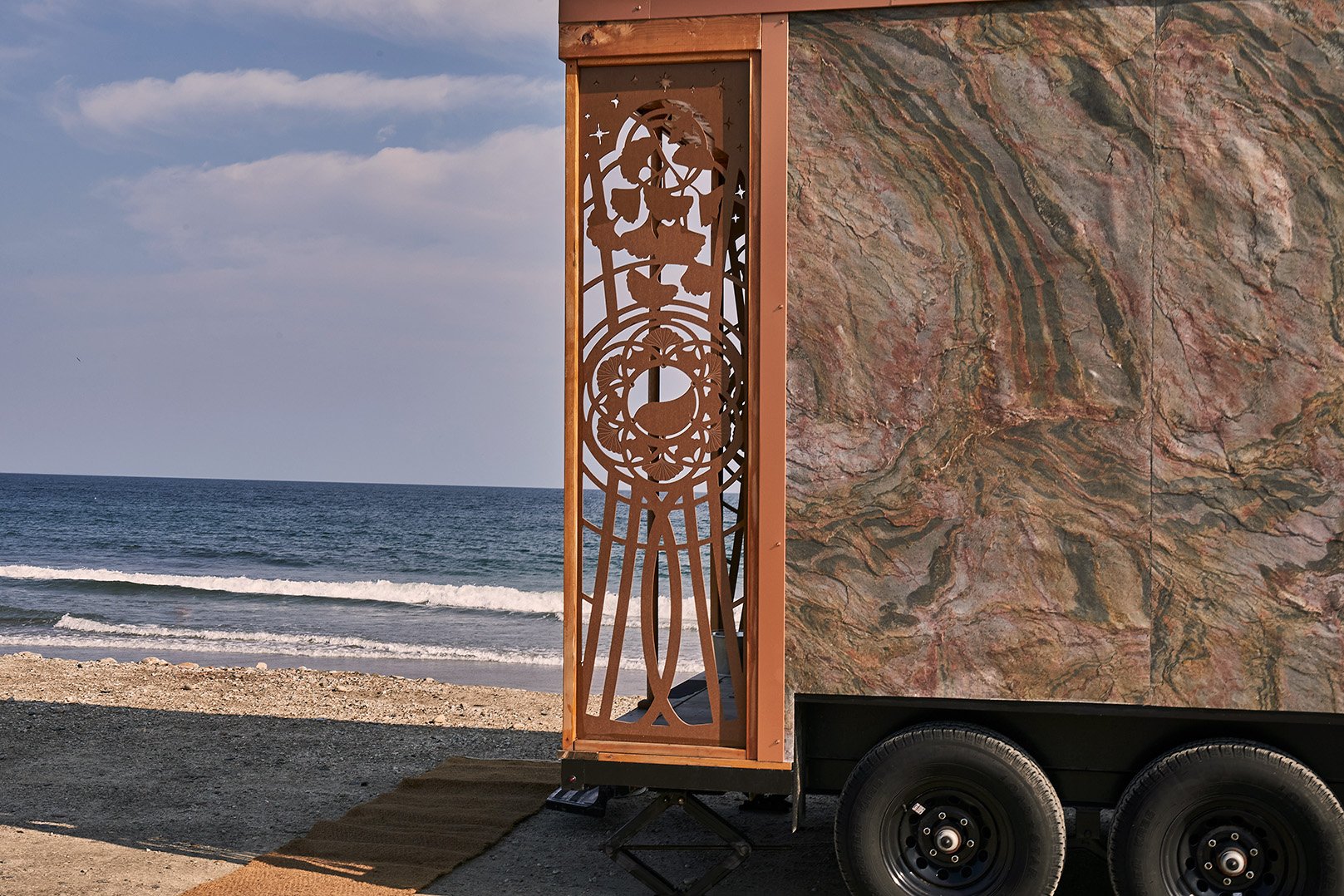 Decorative mobile sauna trailer parked beside a rocky beach and ocean