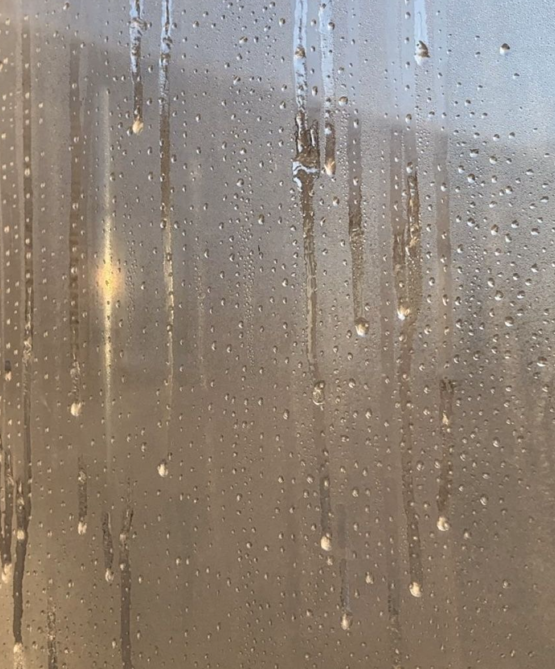 Rain droplets and vertical water streaks on a window with blurred warm light behind it