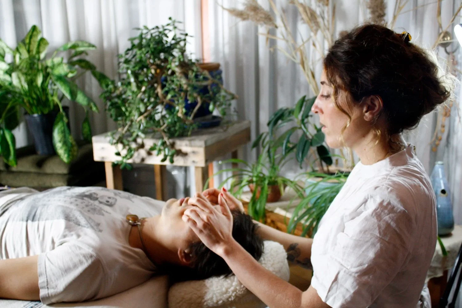 Kayla Sibilia providing crainosacaral therpay to a person lying on a treatment table in a plant-filled room