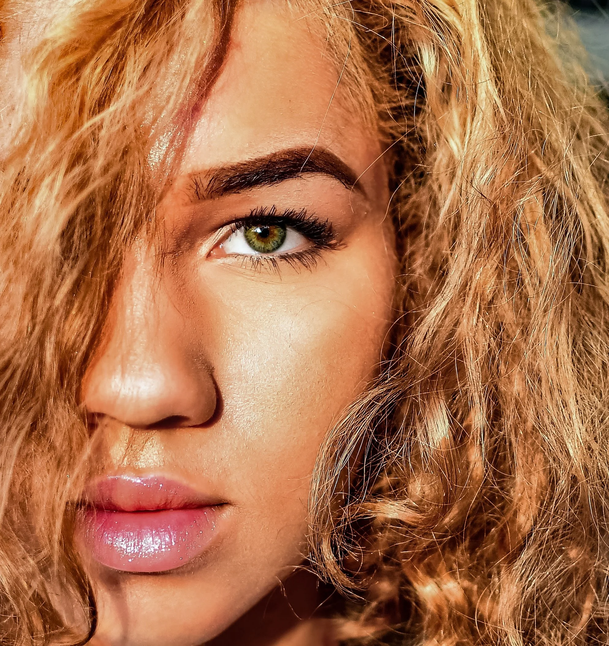 Close-up of a woman's eye with green iris, makeup, and curly blonde hair partially covering her face.