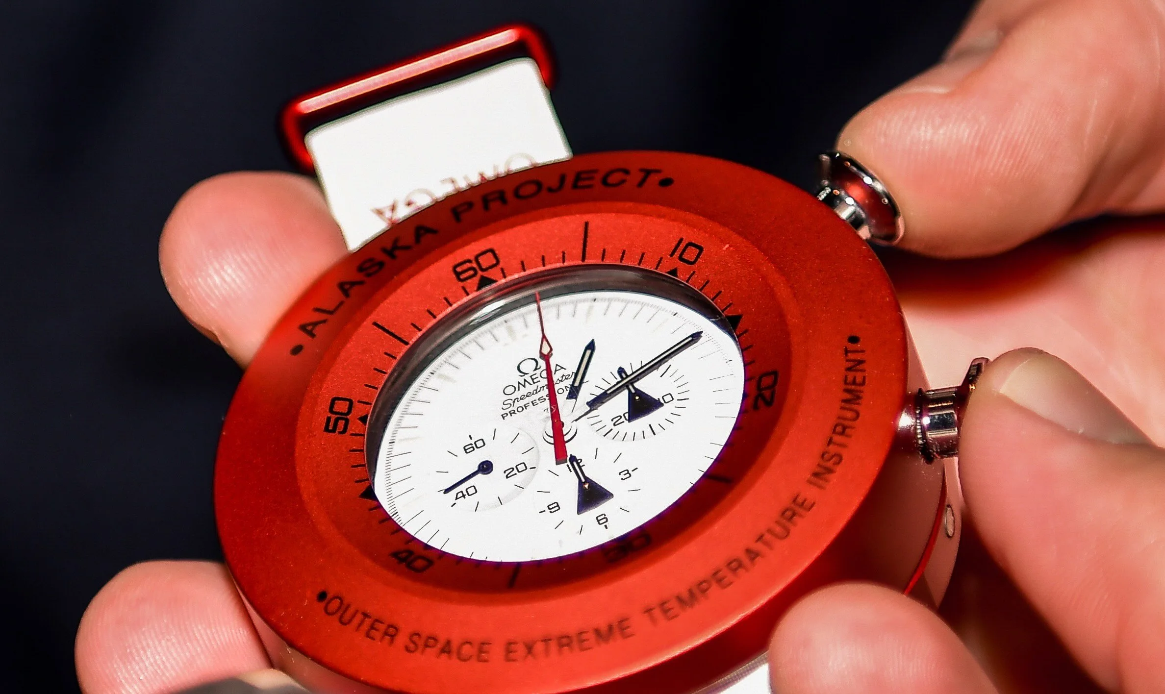 A person holding an orange Omega Speedmaster chronograph watch with a white face and black numbers, with a NASA logo on the face, against a dark background.