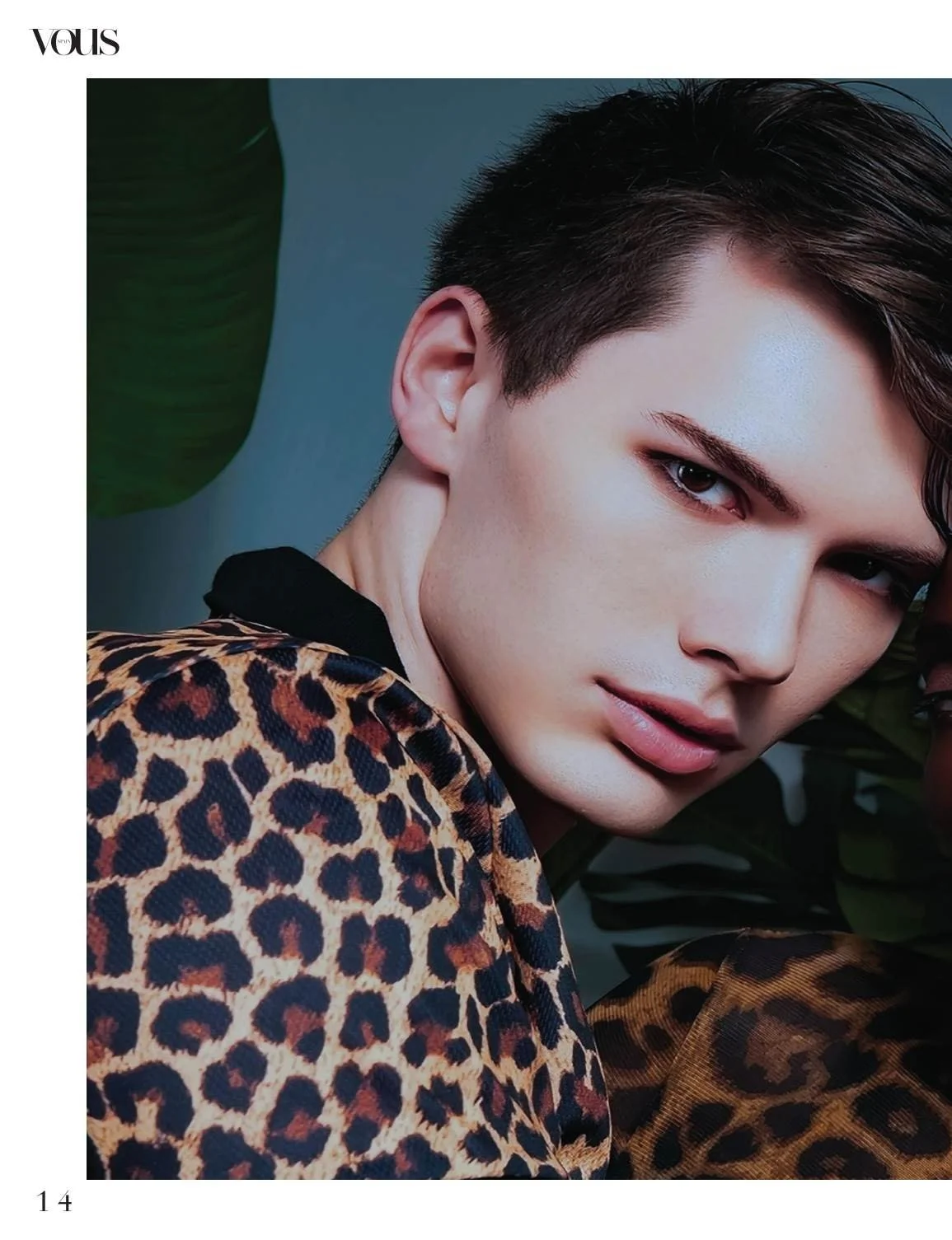 Close-up of a woman with short dark hair, wearing a leopard print jacket, posing against a backdrop with green foliage.