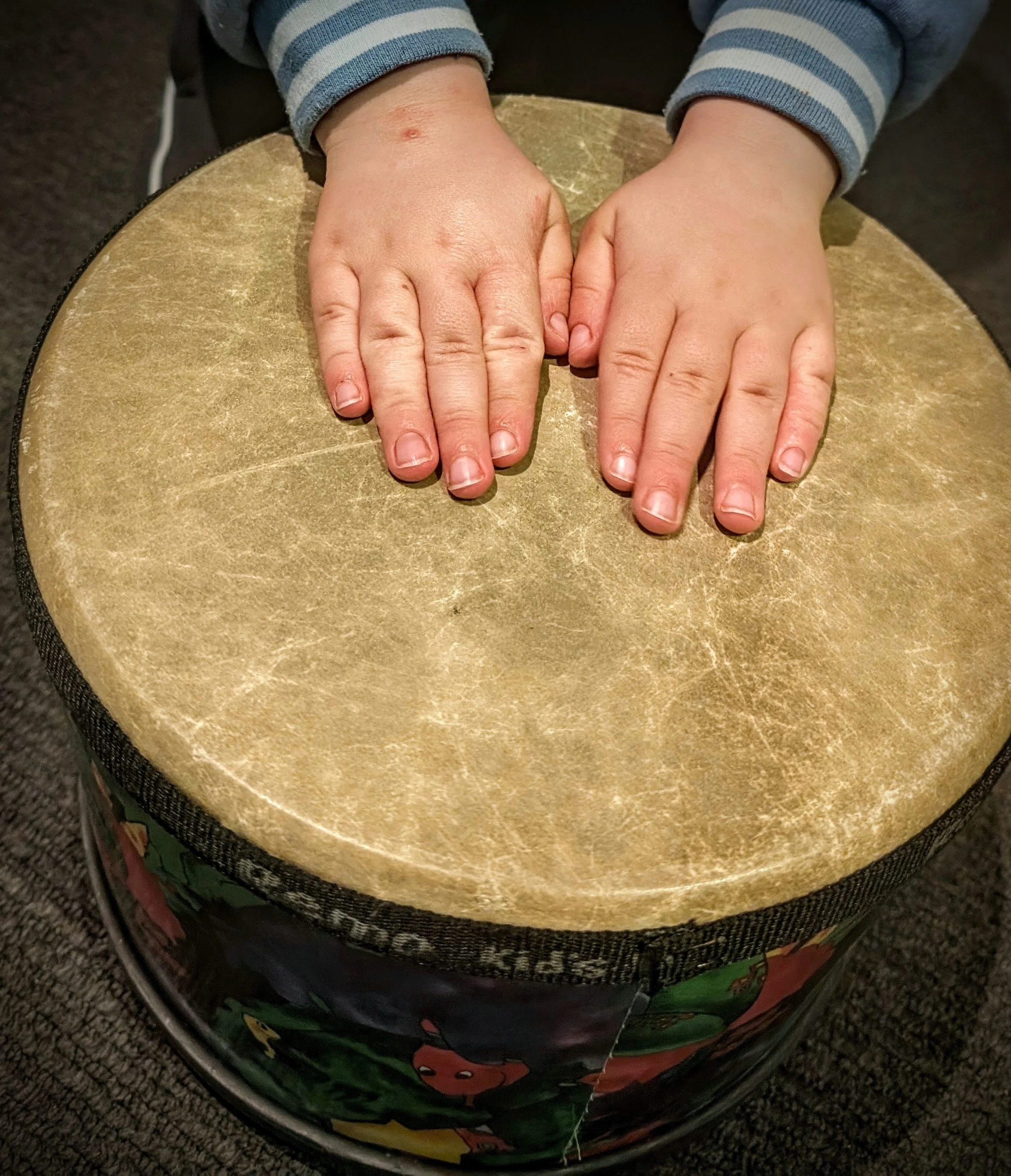 Two hands with different skin tones resting on a circular surface, one hand on each side, with a child's arm in a striped sweater visible in the background.