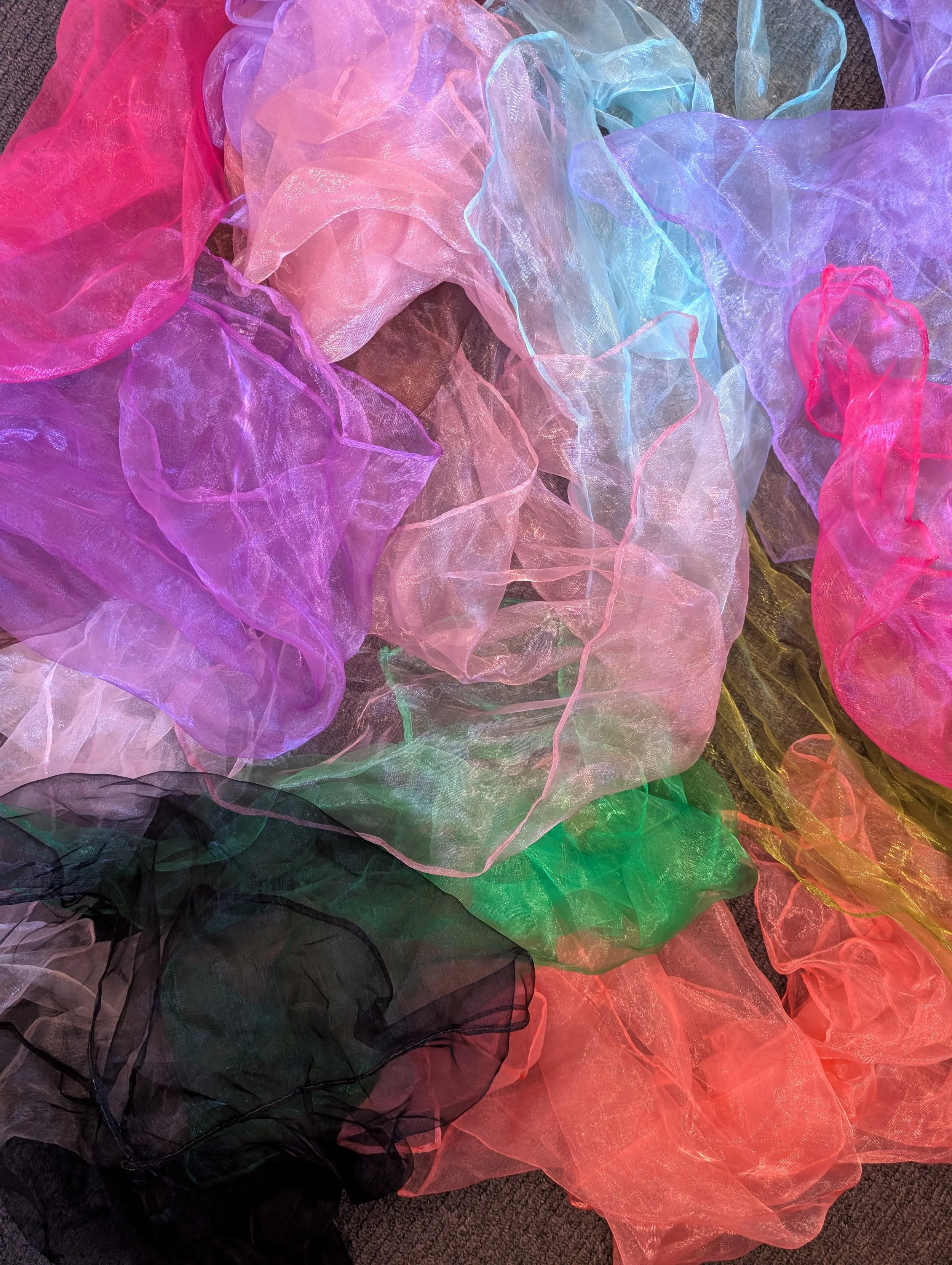 A colorful collection of translucent fabric pieces in pink, purple, blue, green, yellow, and black, spread out on a dark surface.