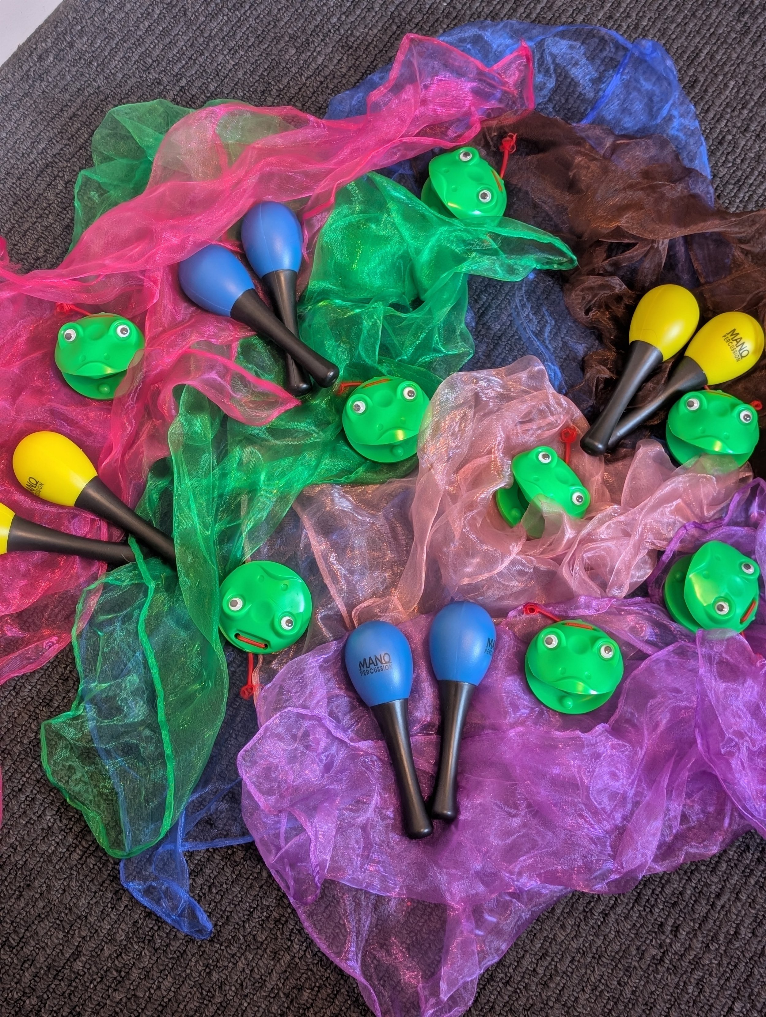 Colorful toy frogs and maracas on multicolored sheer fabric on brown carpet.