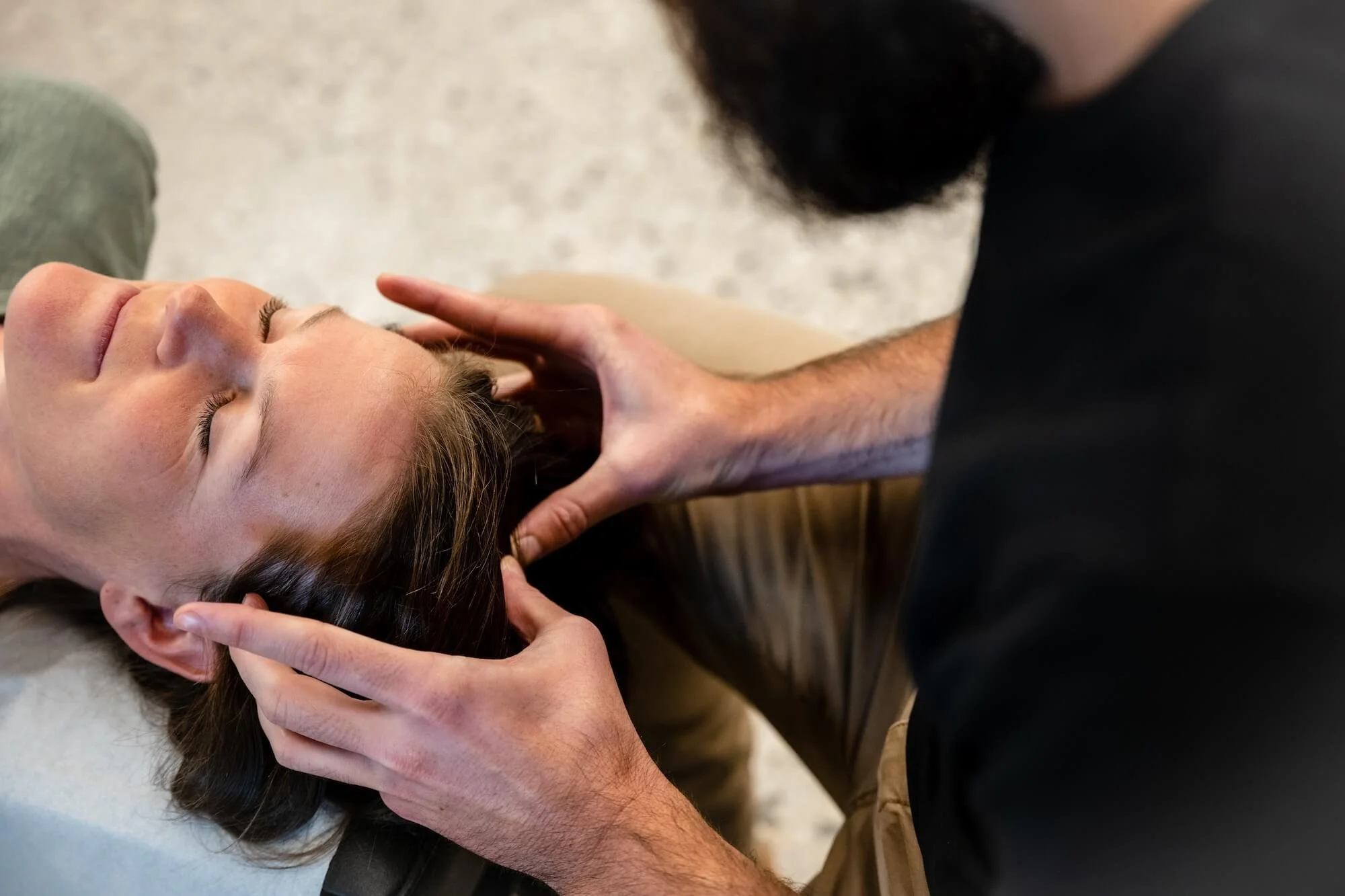 A person lying on their back receiving a chiropractic or massage therapy treatment, with a therapist holding their head and neck gently, in an indoor setting.