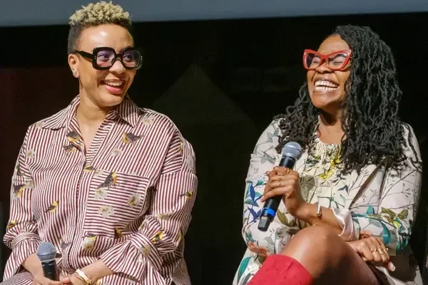 Two women sitting on stage, smiling, and holding microphones, engaged in conversation.