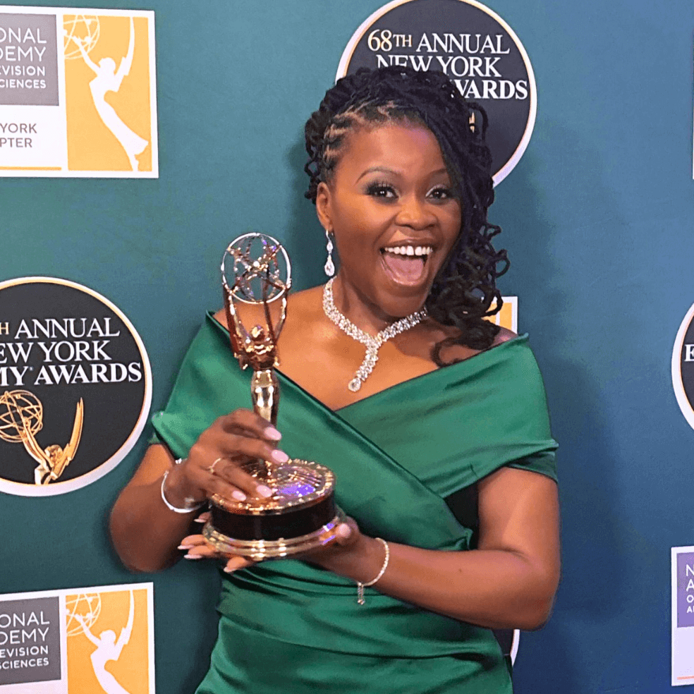 A woman in a green satin dress holding an Emmy award, smiling happily, with a backdrop displaying logos for the 68th Annual New York Emmy Awards and the National Academy of Television Arts & Sciences.