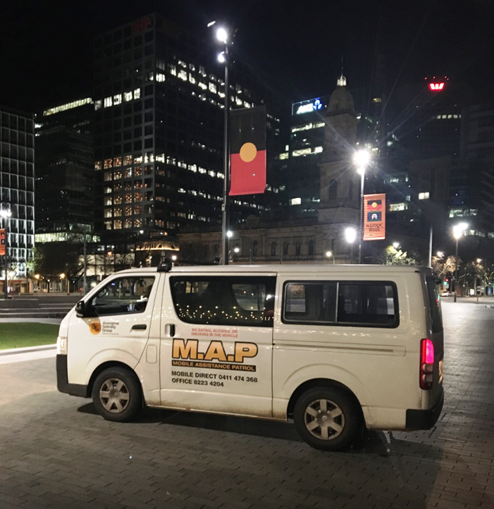 White van with 'M.A.P. Mobile Assistance Patrol' logo parked on a city street at night, surrounded by tall office buildings illuminated with lights.