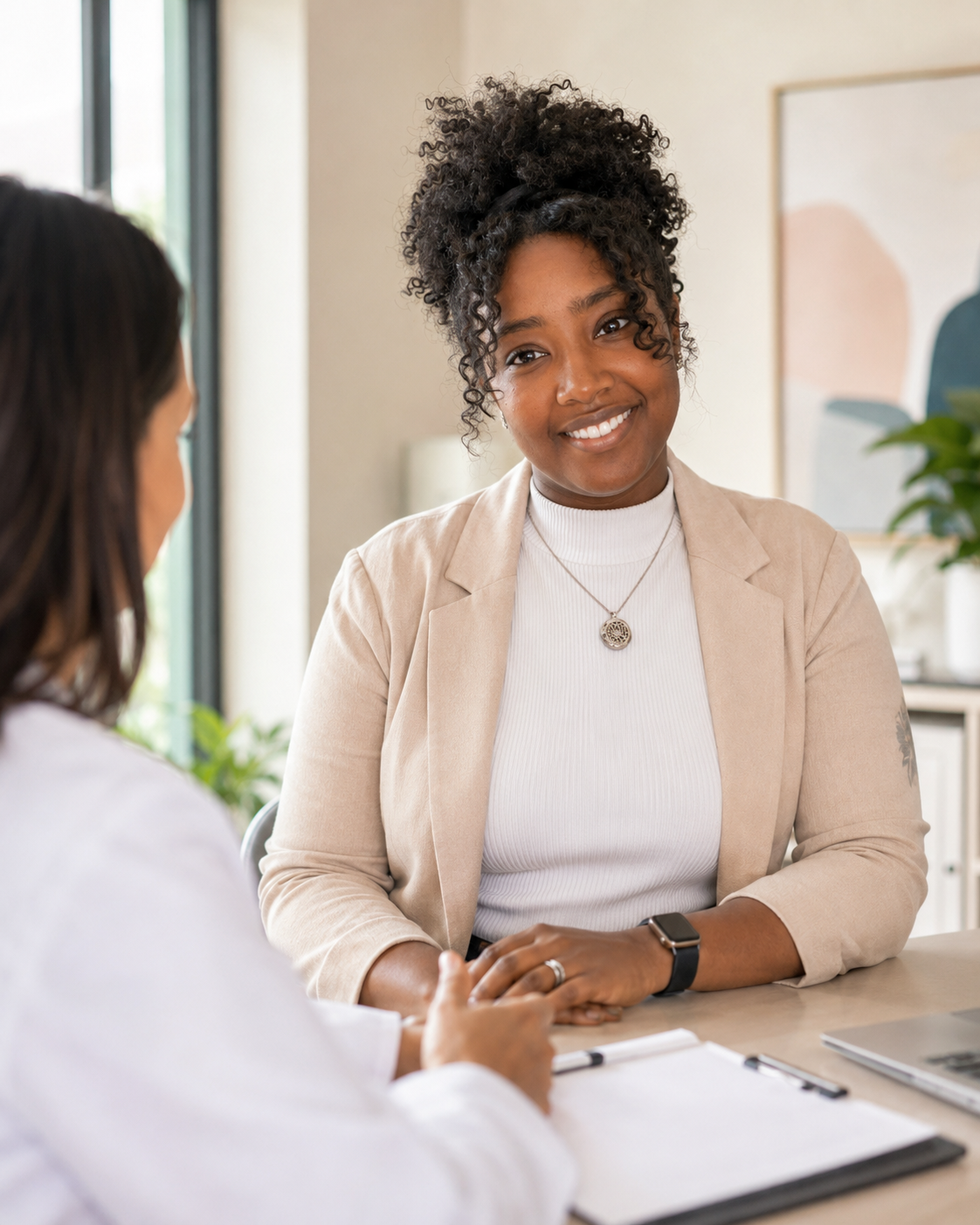 Two women engaged in a conversation in an office setting, one smiling and the other listening.