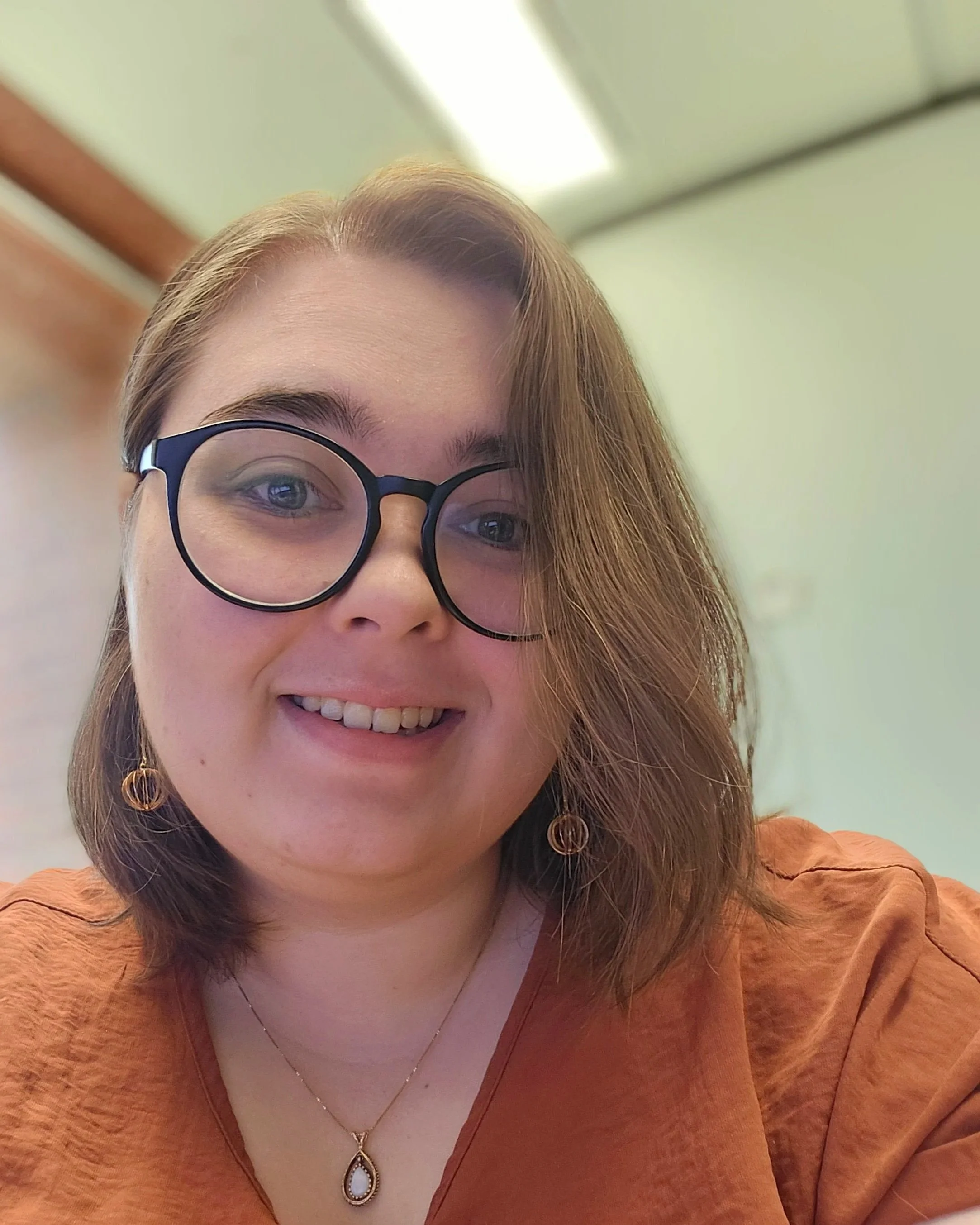 Woman with shoulder length brown hair, glasses, and smiling.