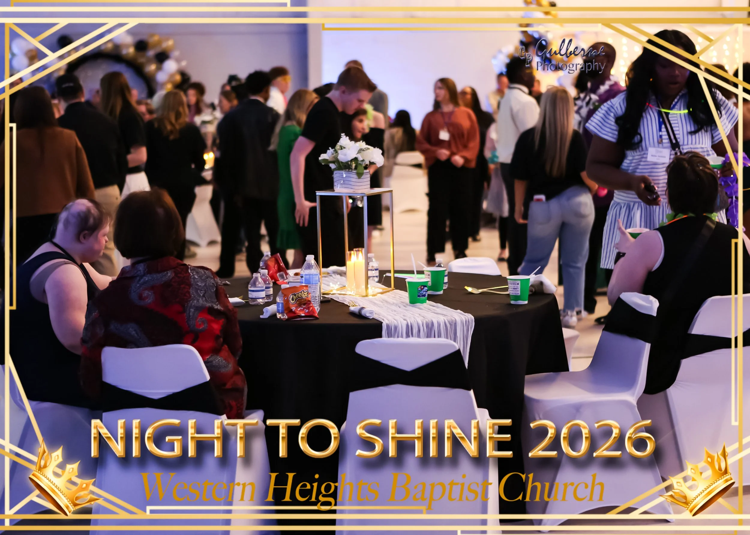 Scene from the Night to Shine 2026 event at Western Heights Baptist Church, featuring a crowded indoor space with decorated tables, people socializing, and a floral centerpiece on a table