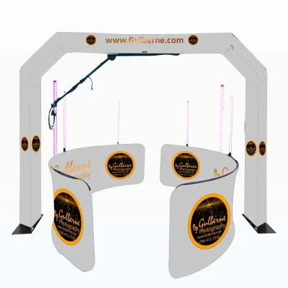 Photo of a photo booth set-up with a white archway and circular side panels, branded with 'Gullherme Photography' logos and website, featuring a white counter and pink light strips.