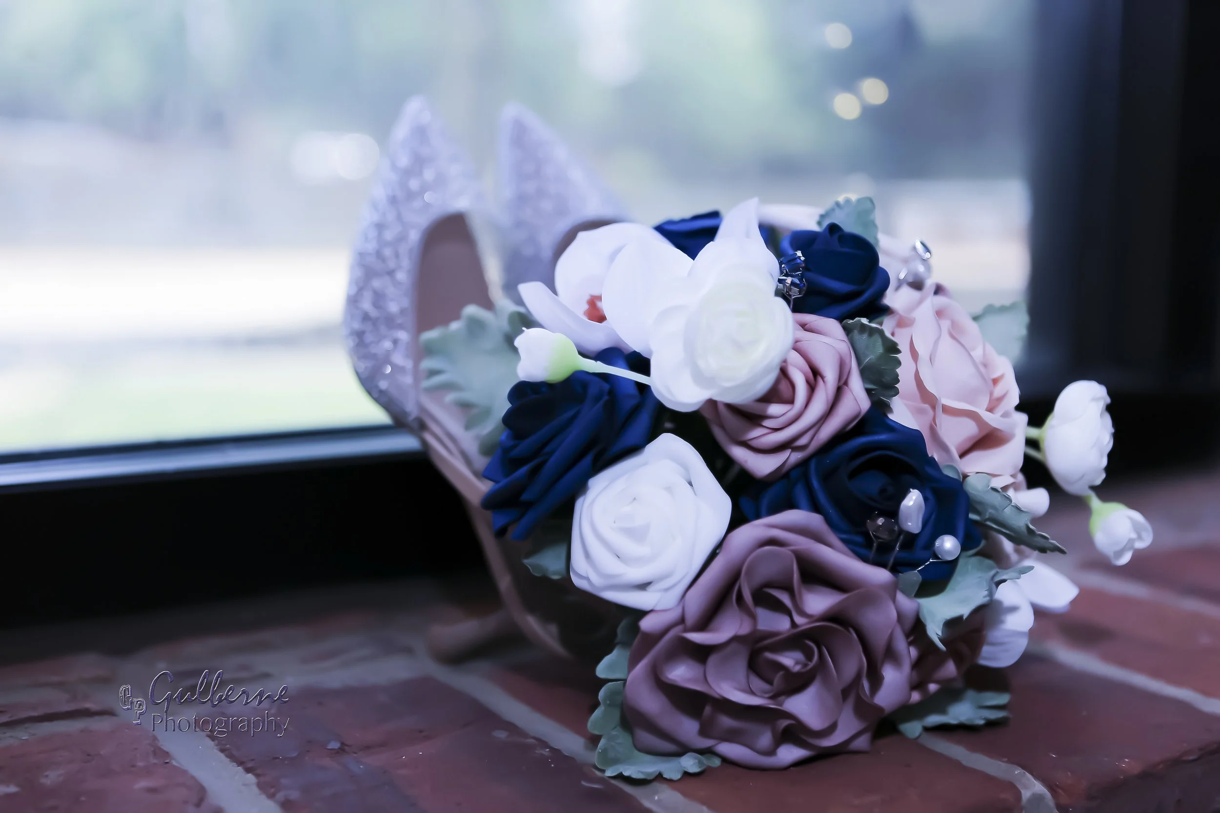 A colorful bouquet of fabric flowers, including roses and other blooms, is placed on a wooden surface near a window.
