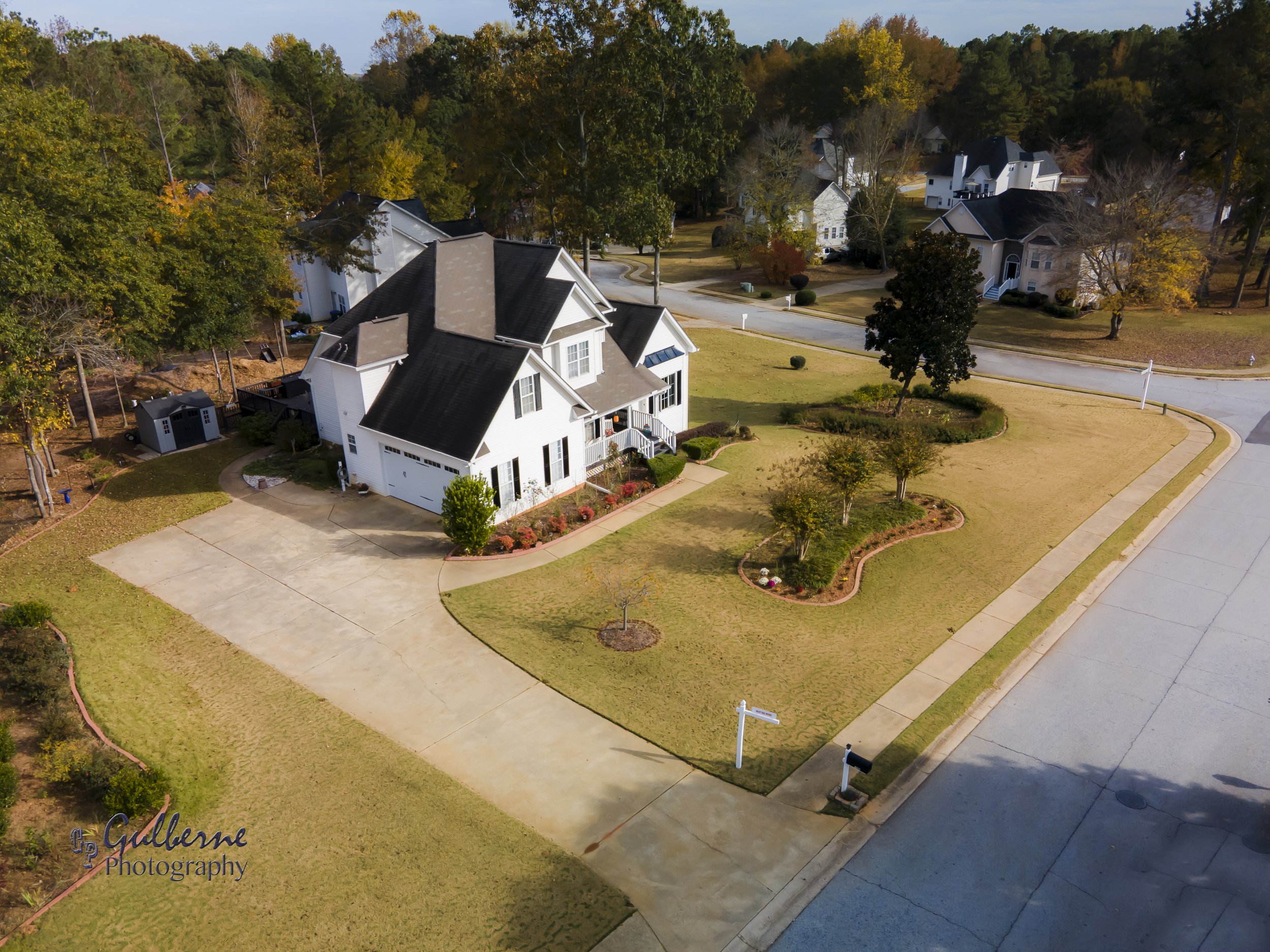 An aerial view of a residential neighborhood with a large white house and well-maintained lawns, trees with fall foliage, and curved roads.