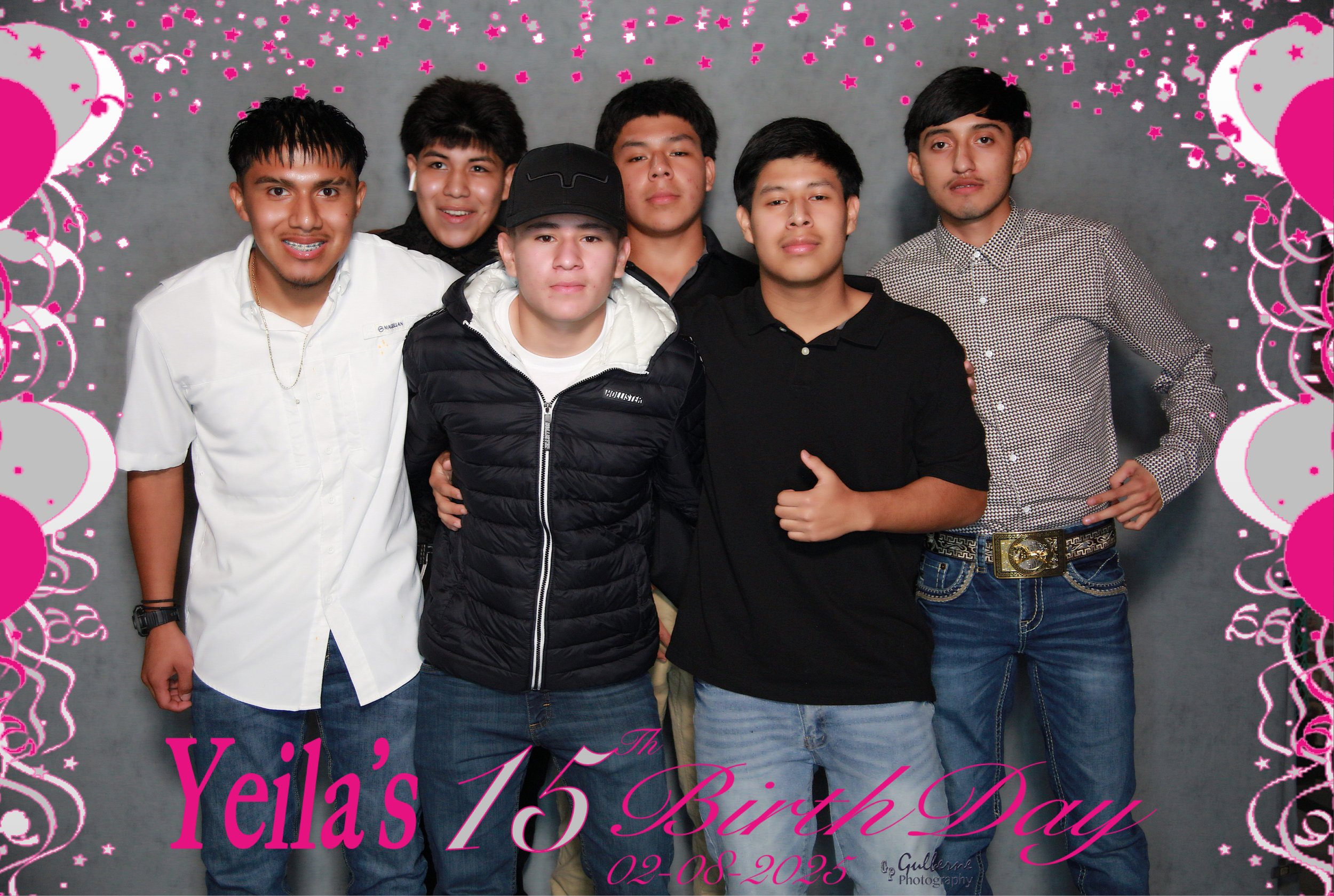 Group of six young men standing together in front of a gray background decorated with pink and white floral patterns and balloons, celebrating a birthday on February 8, 2025.