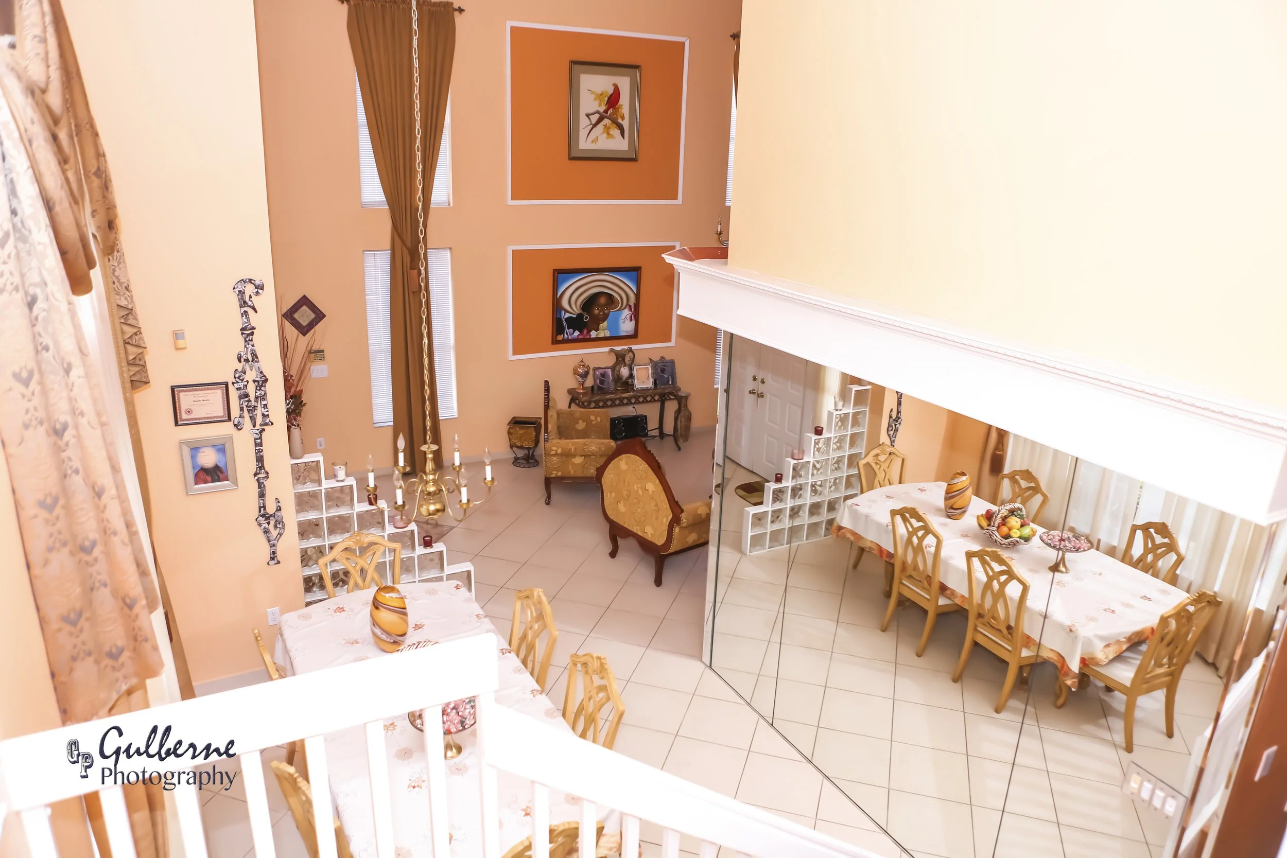 Interior view of a living and dining room with peach-colored walls, decorated with framed artwork, a table with a floral tablecloth, and multiple chairs, with a chandelier hanging from the ceiling.