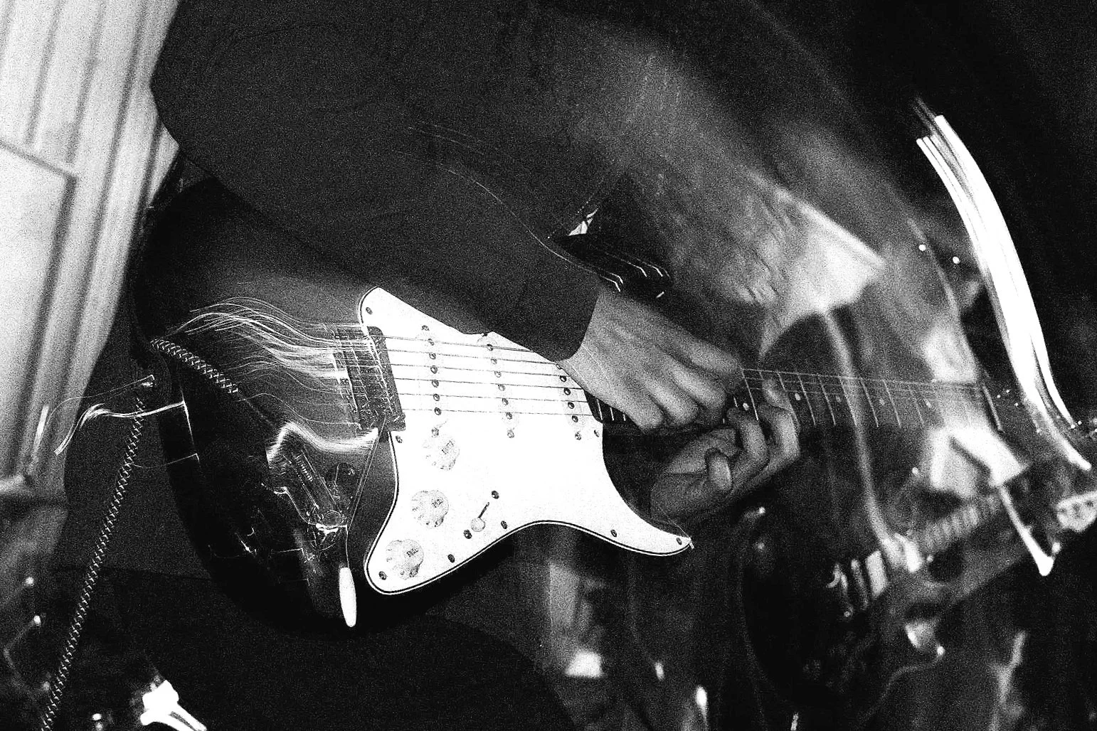 A person playing an electric guitar in black and white, with their hand on the fretboard and the body of the guitar visible.