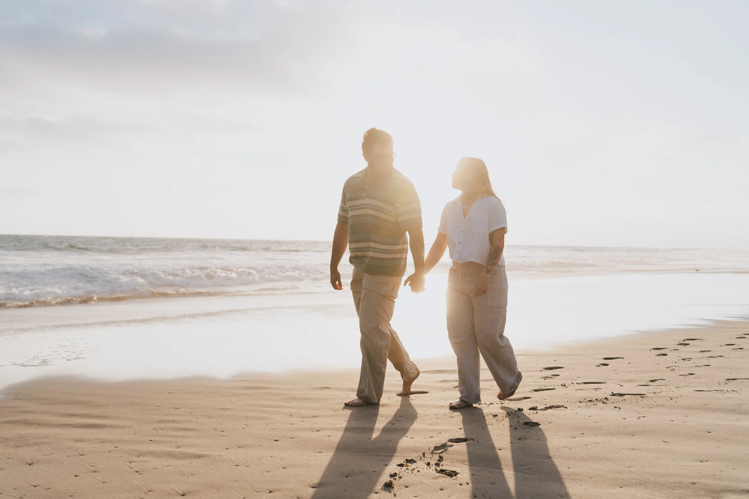 A couple holding hands walking on the beach during sunset.