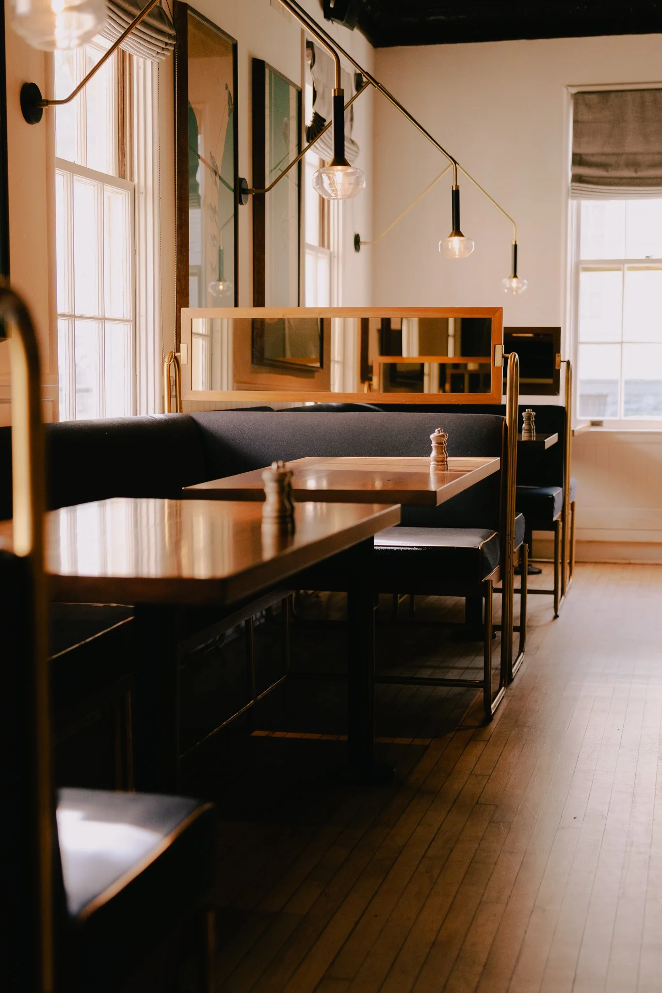 Interior of a restaurant or cafe with wooden tables, black seating, large picture windows, and modern hanging light fixtures.