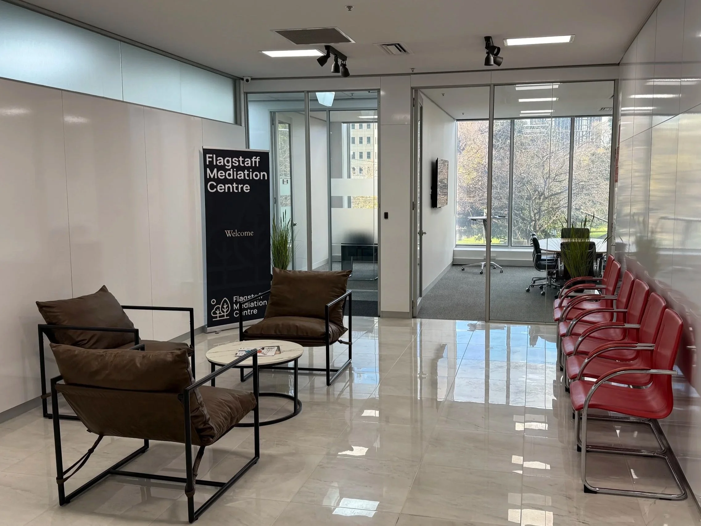 Flagstaff Mediation Centre Melbourne, view of main reception or meeting area, with chairs, a small table, and a sign welcoming visitors, large windows showing trees outside in Flagstaff Gardens.