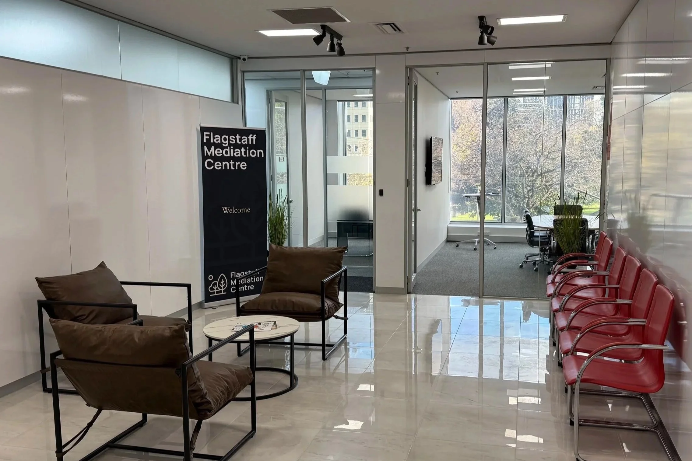 Flagstaff Mediation Centre main reception area with seating area, chairs, plants, and large windows showing trees outside.