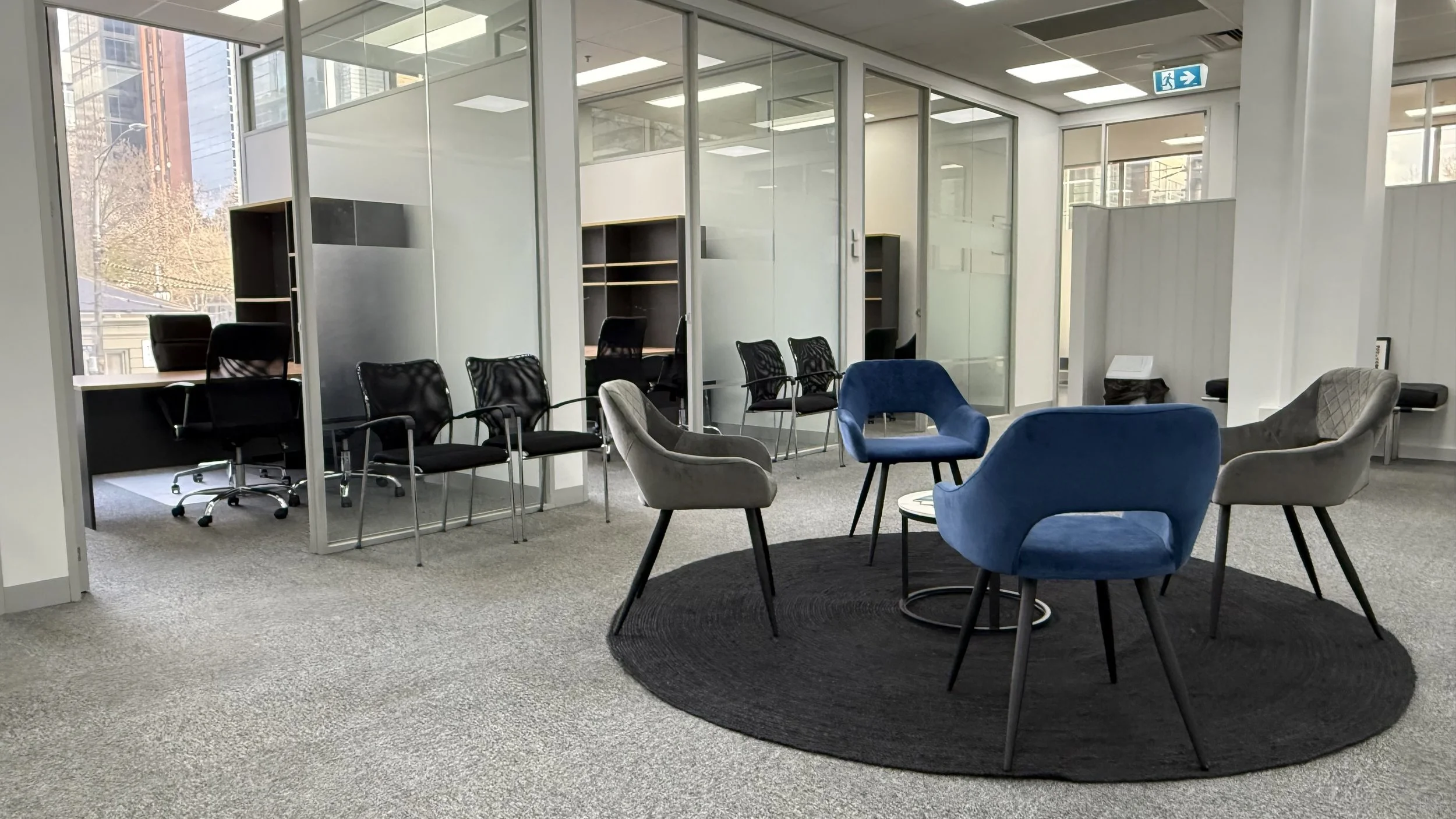 Second waiting area at Flagstaff Mediation Centre, with access to glass partitioned breakout rooms in the background, large windows showing city buildings facing the Former Mint, County and Supreme Courts